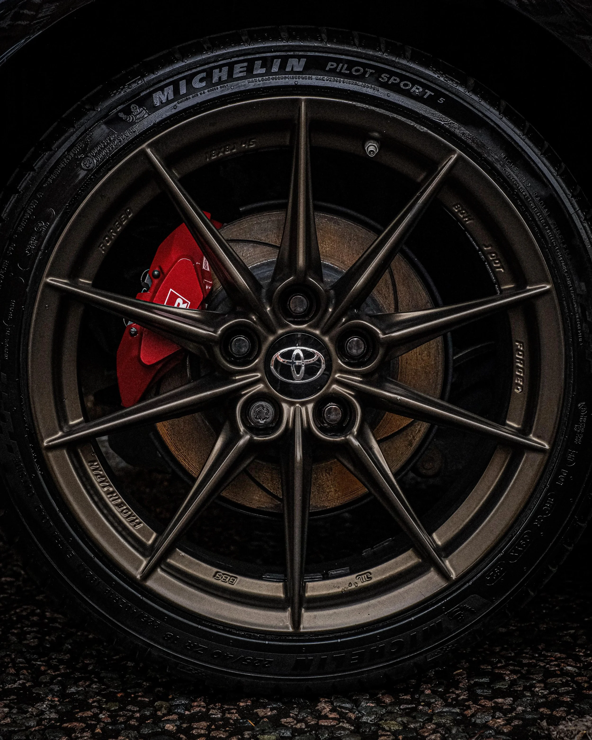 Close-up of a car wheel featuring a Michelin Pilot Sport 5 tire, a metallic rim with multiple spokes, red brake caliper, and Toyota emblem at the center.