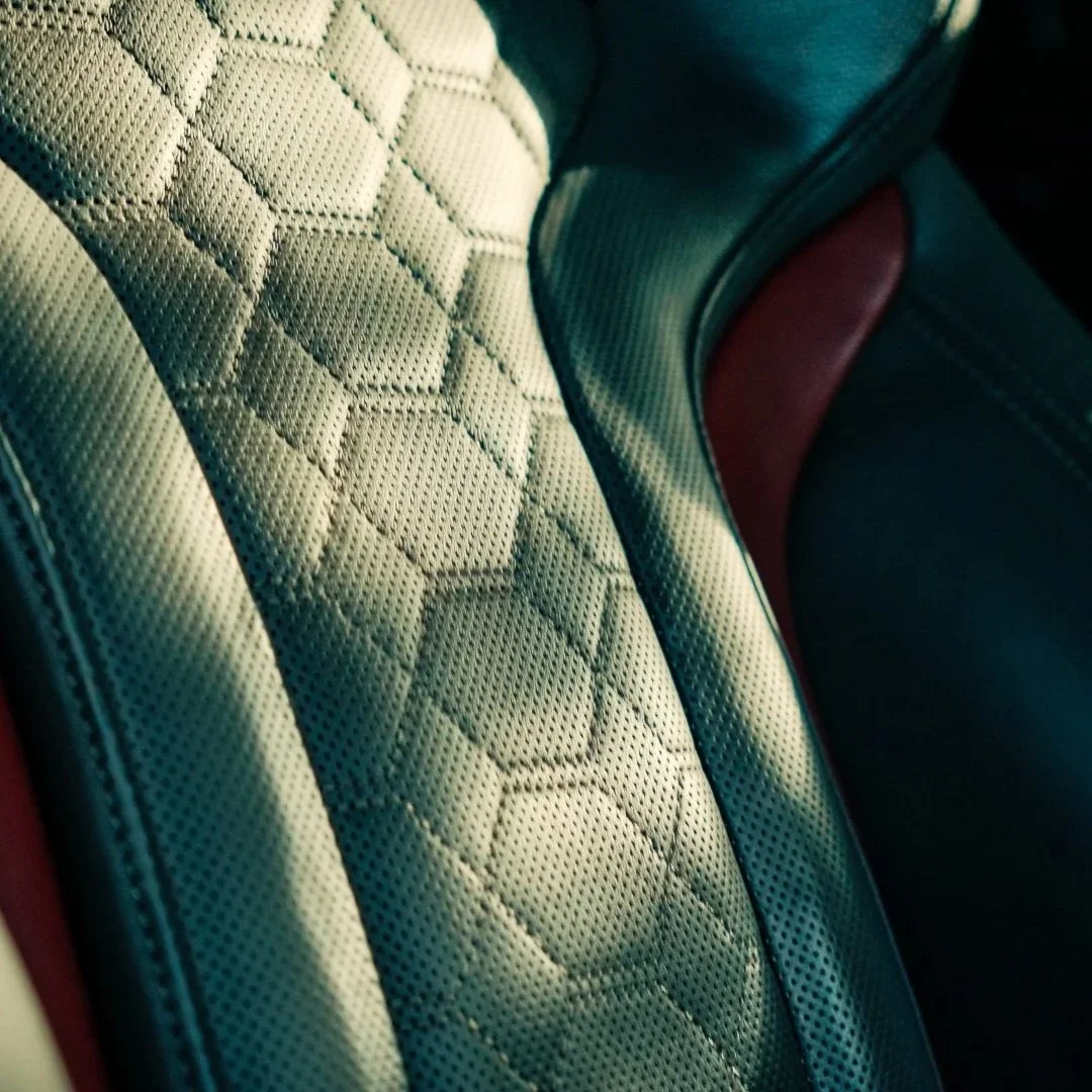 Close-up of a car seat with white and black leather upholstery, featuring a hexagonal pattern and red accents.