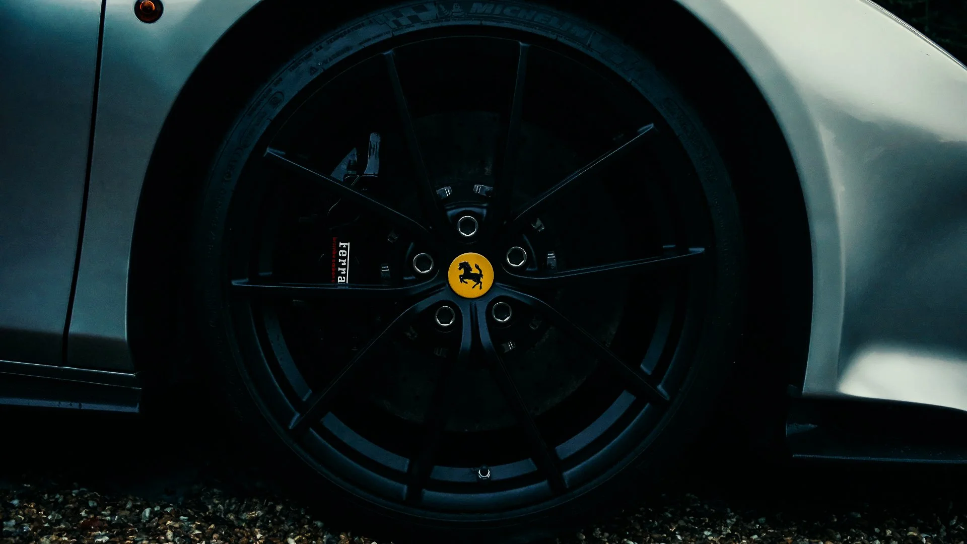 Close-up of a Ferrari sports car wheel with black rim, yellow center cap with Ferrari logo, and white body panel.