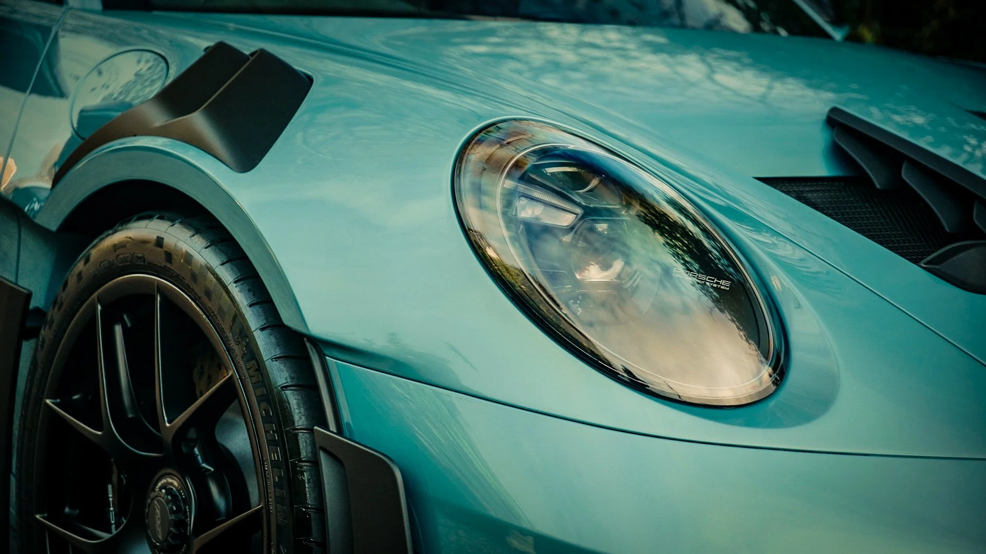 Close-up of a blue sports car with a sleek headlight and a black tire with Mercedes-Benz rim.