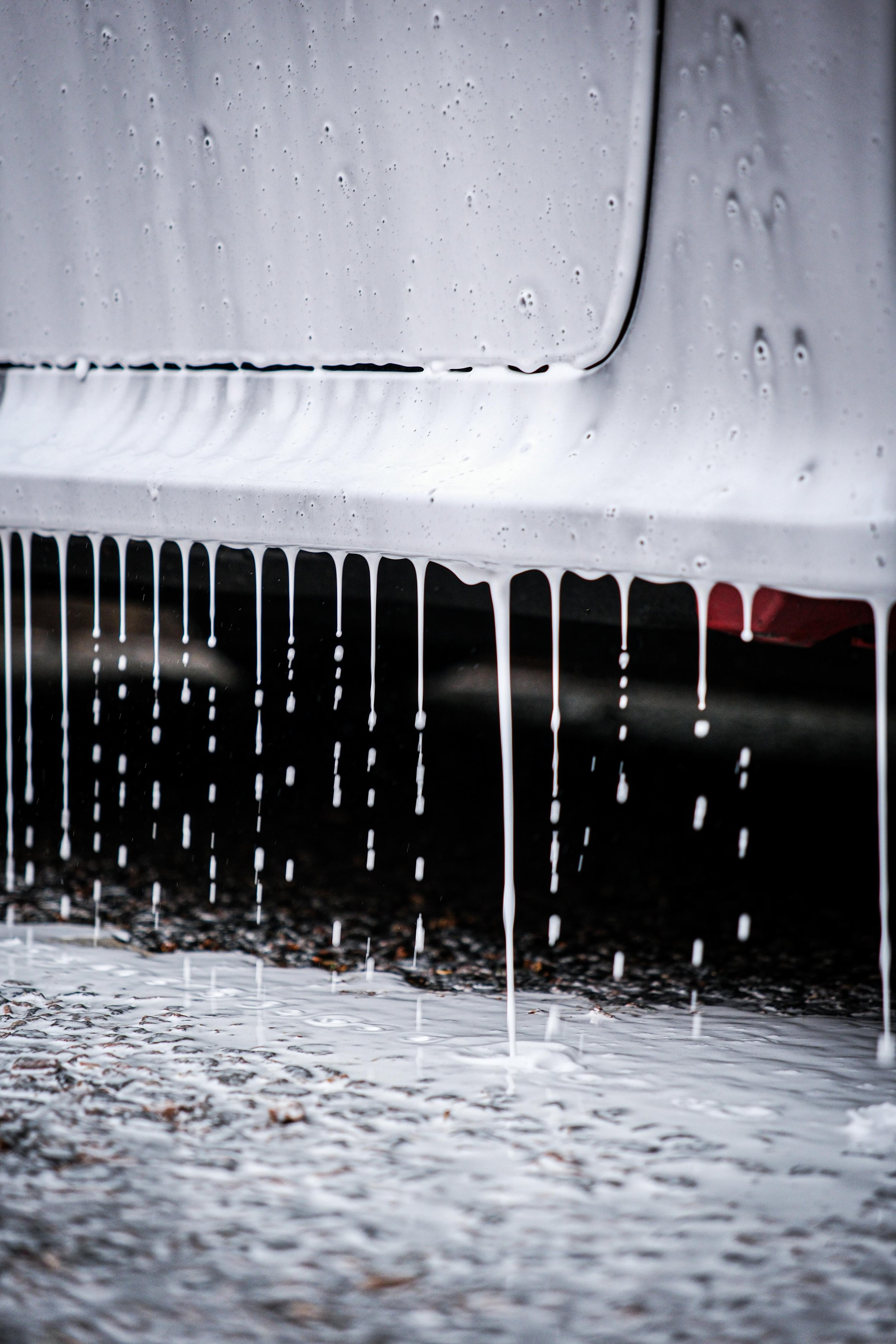 White liquid dripping from the underside of a white car onto a wet ground.