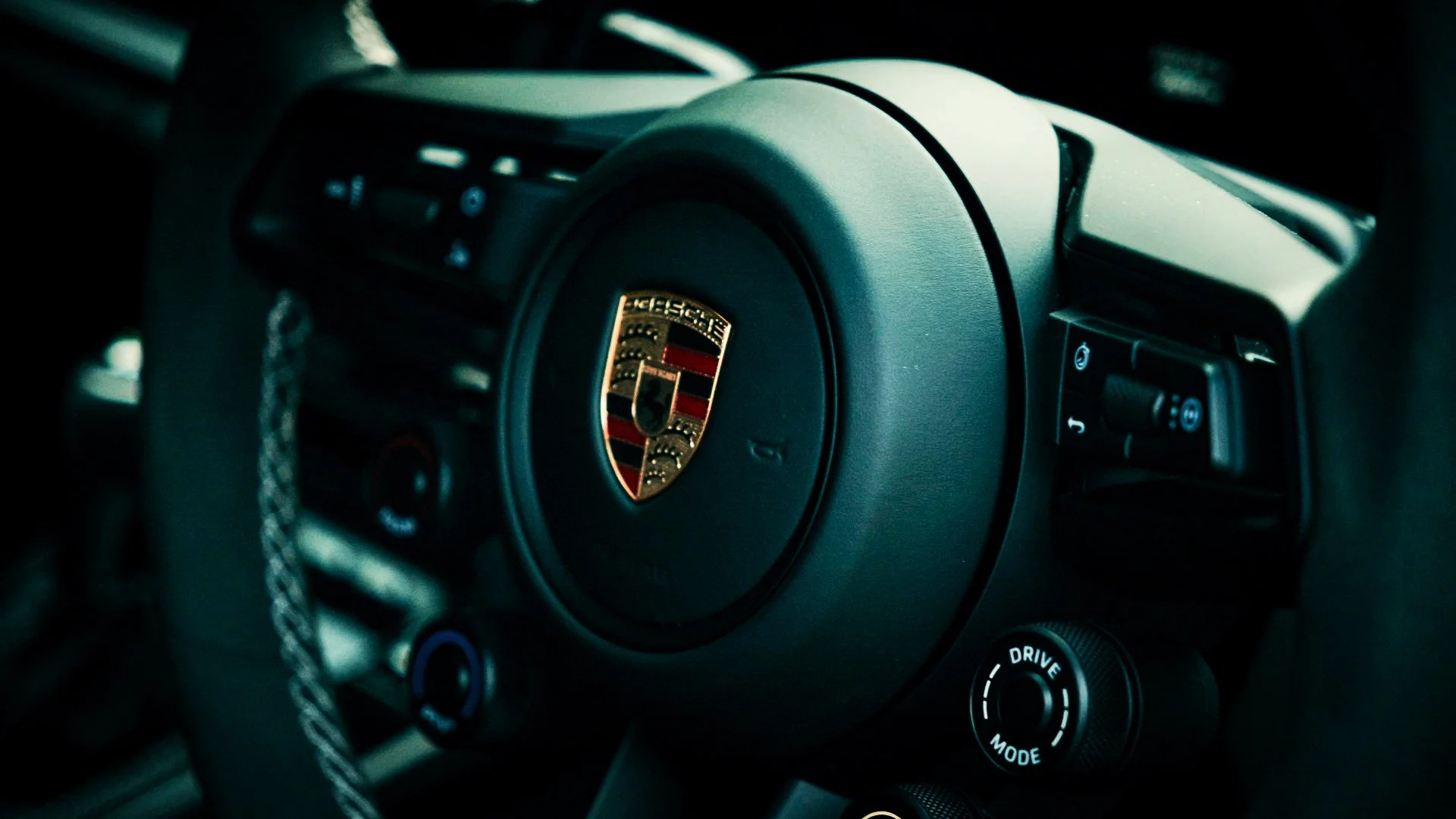 Close-up of the steering wheel of a Porsche car, featuring the Porsche emblem in the center.
