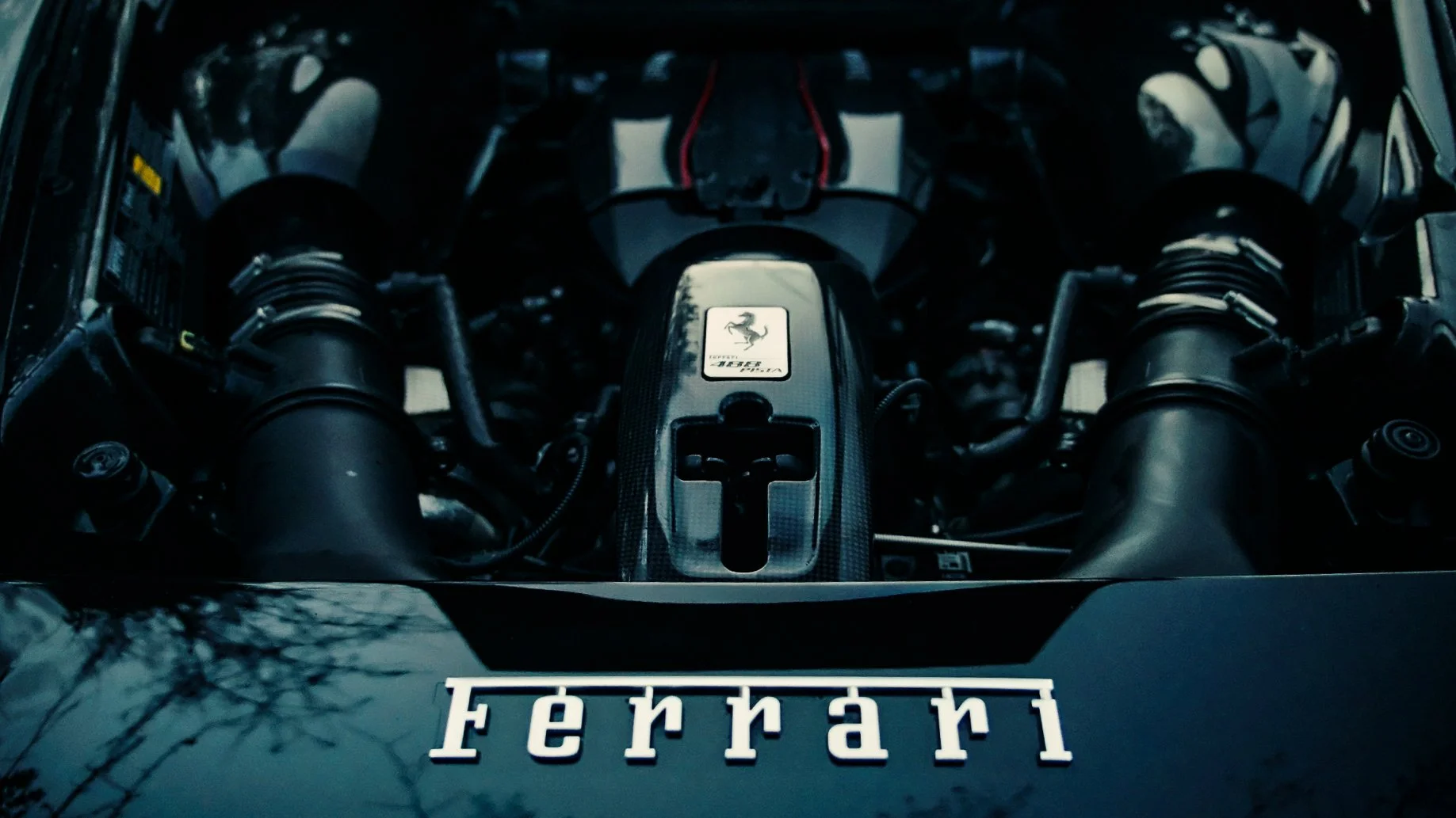 Close-up view of a Ferrari engine with a Ferrari logo and a prancing horse emblem, showing various engine components and pipes.