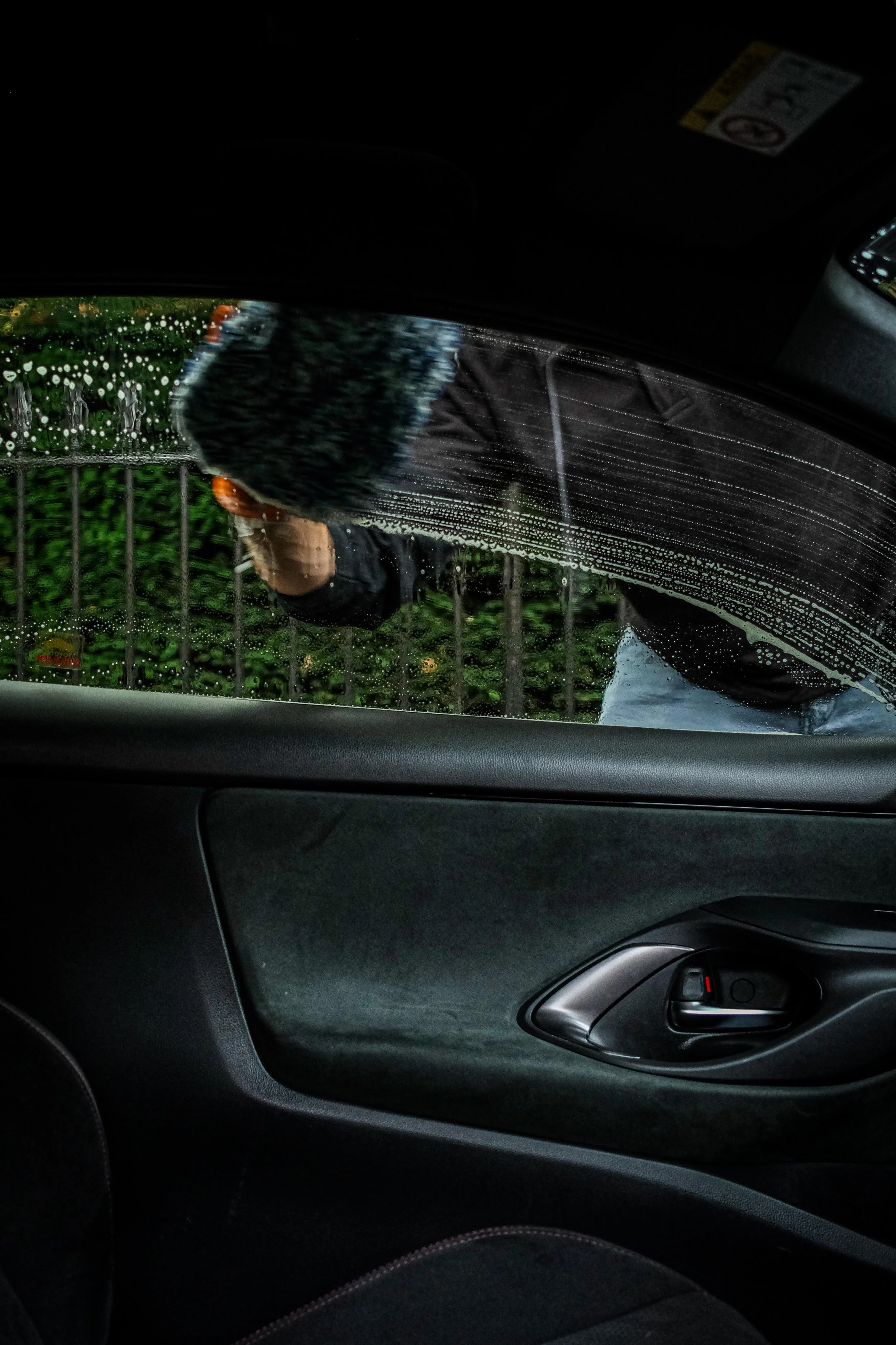 Person washing the car window from outside, with water and soap on the glass, seen from inside the vehicle.