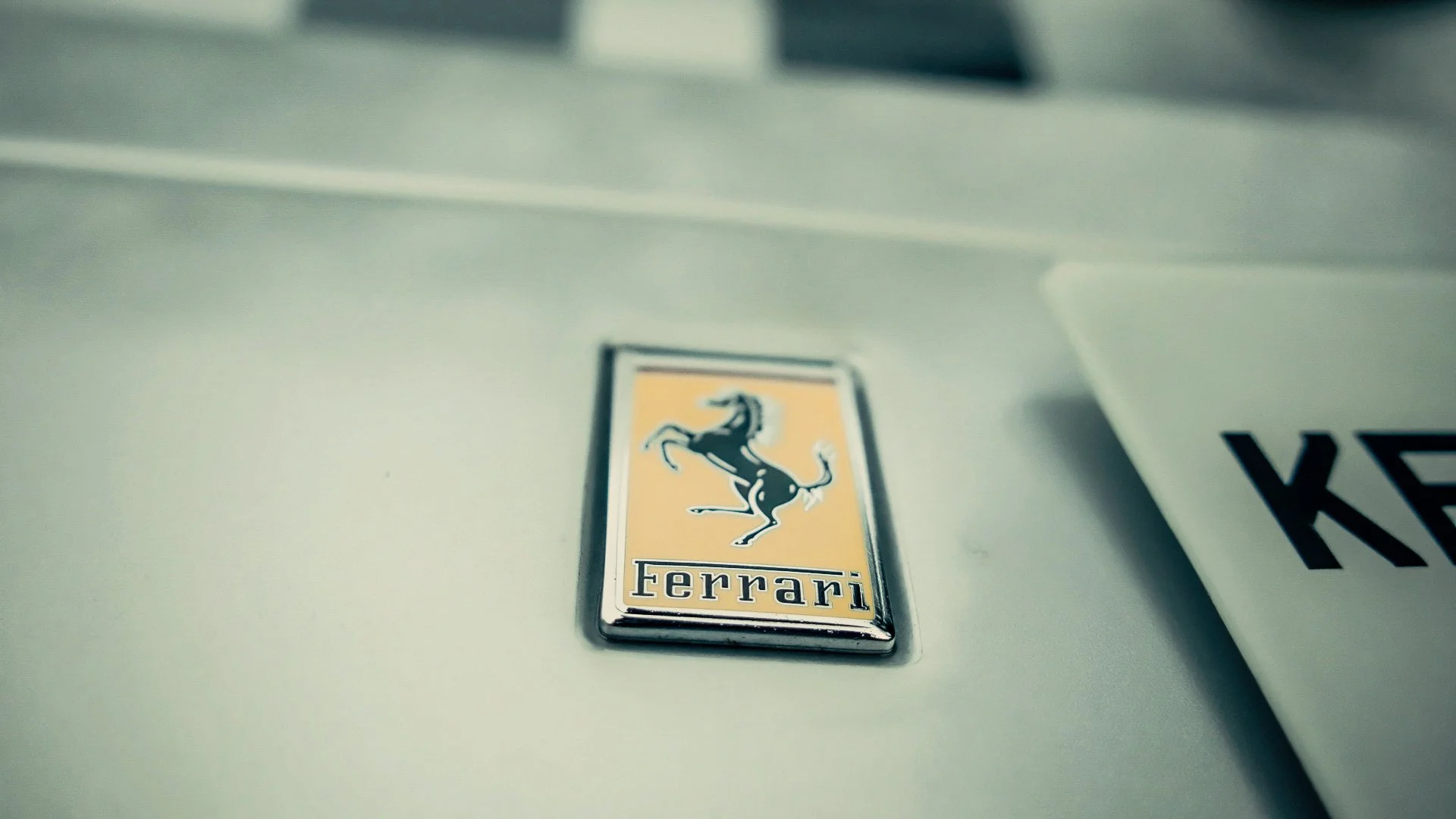 Close-up of a Ferrari logo emblem on a car's metallic surface, with part of a document or paper nearby.