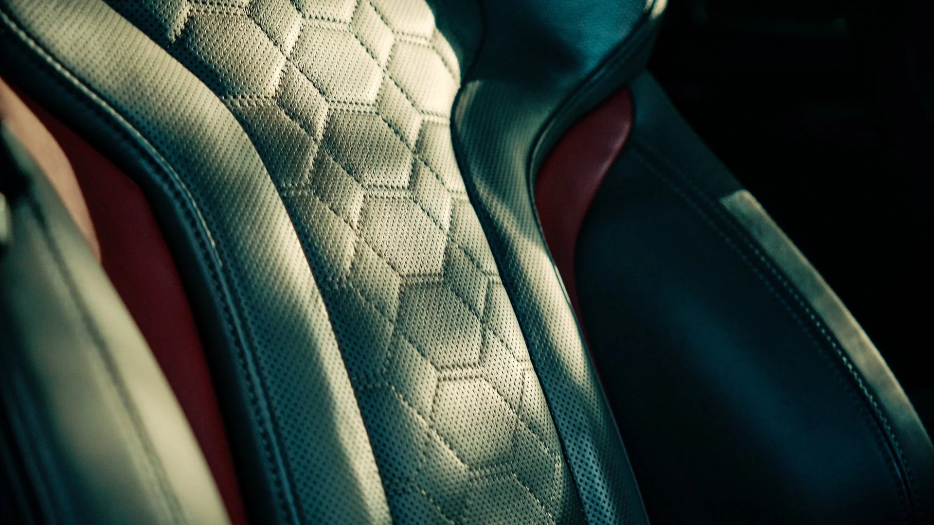 Close-up of a car seat with a quilted pattern, black and red leather accents, and detailed stitching.