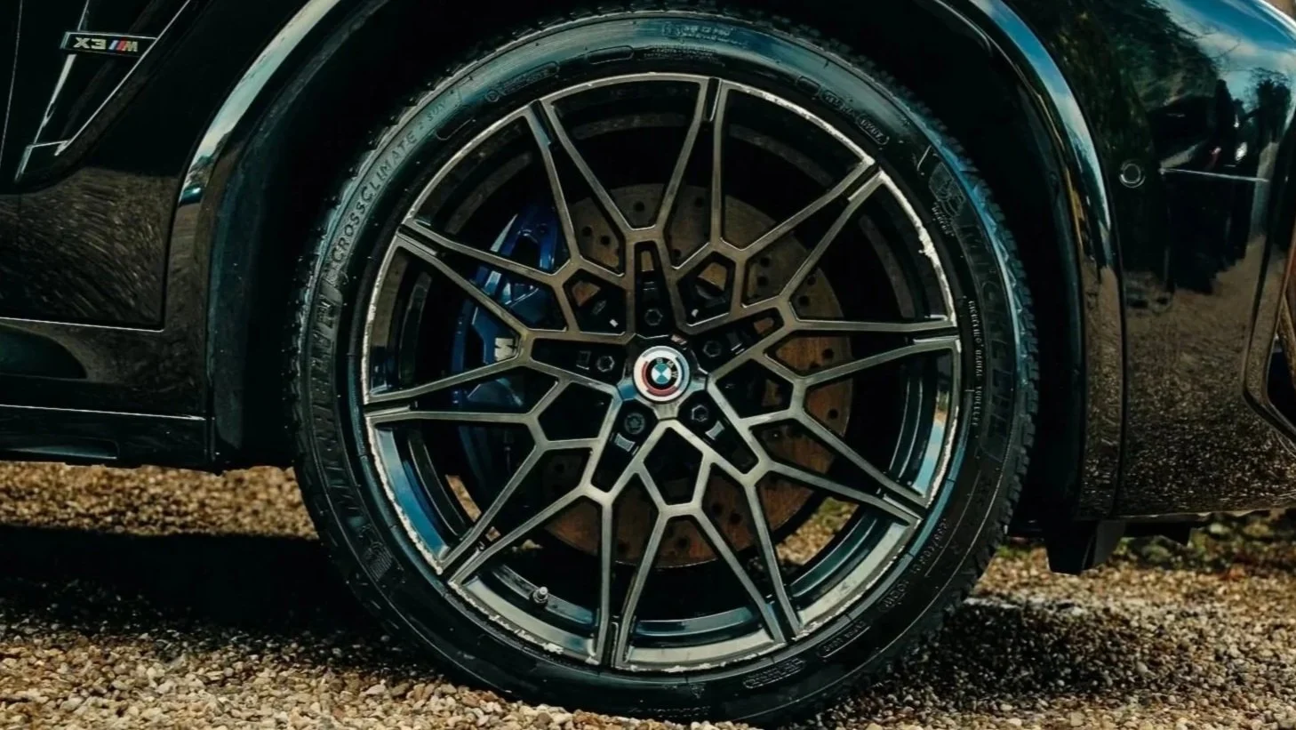 Close-up of a black BMW car wheel with a detailed rim and BMW logo in the center, parked on gravel.
