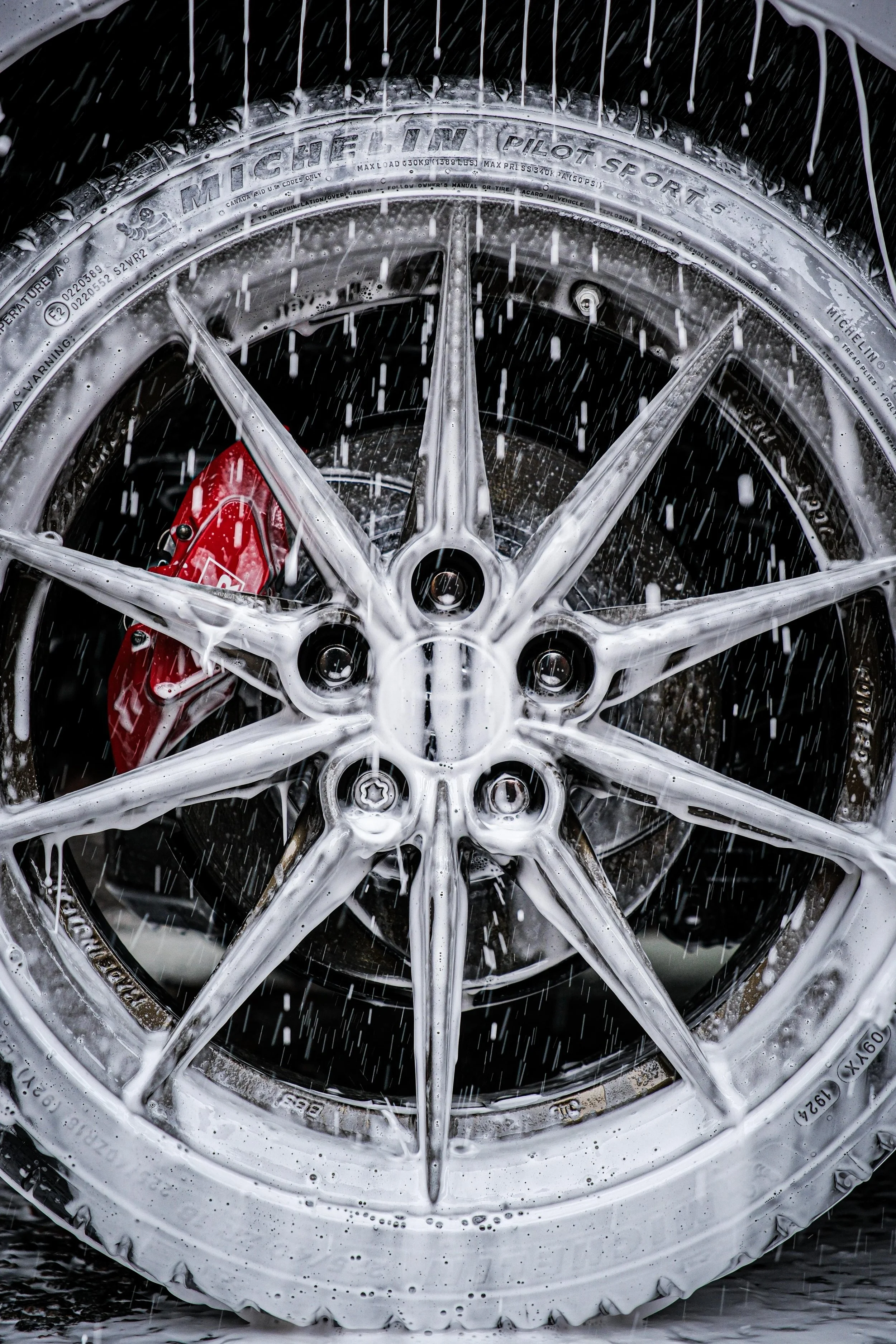 Close-up of a car wheel being washed, with soap suds and water splashing.