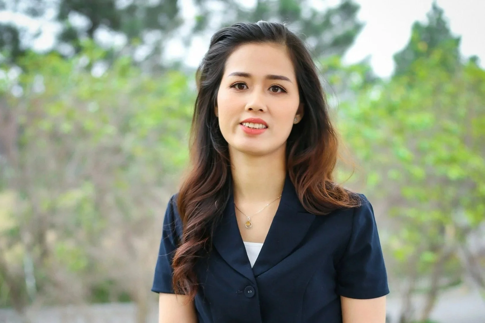 Young woman with curly hair in a bun, wearing glasses, a denim shirt, and a red and white striped t-shirt, smiling at the camera.