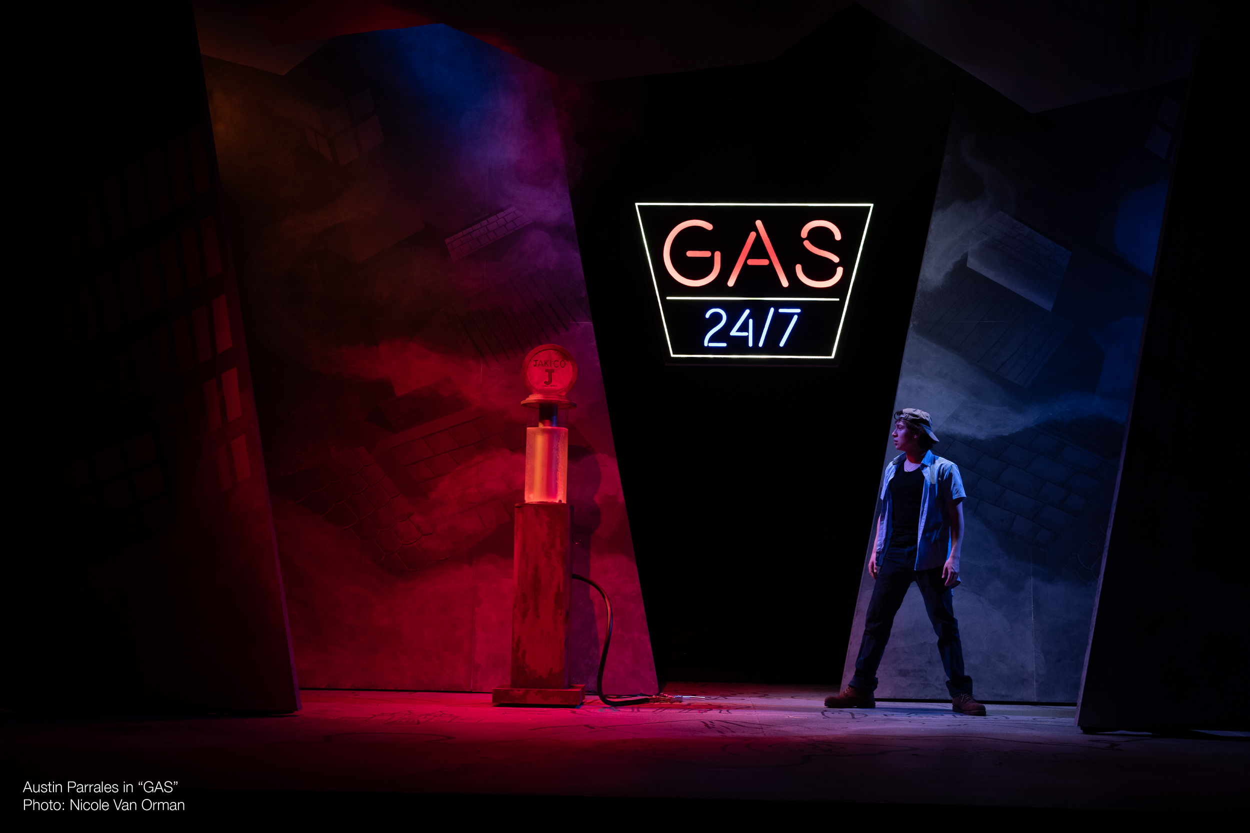 A person standing near a neon sign that reads 'GAS 24/7' in a dark, theatrical setting with colorful lighting and abstract backgrounds.