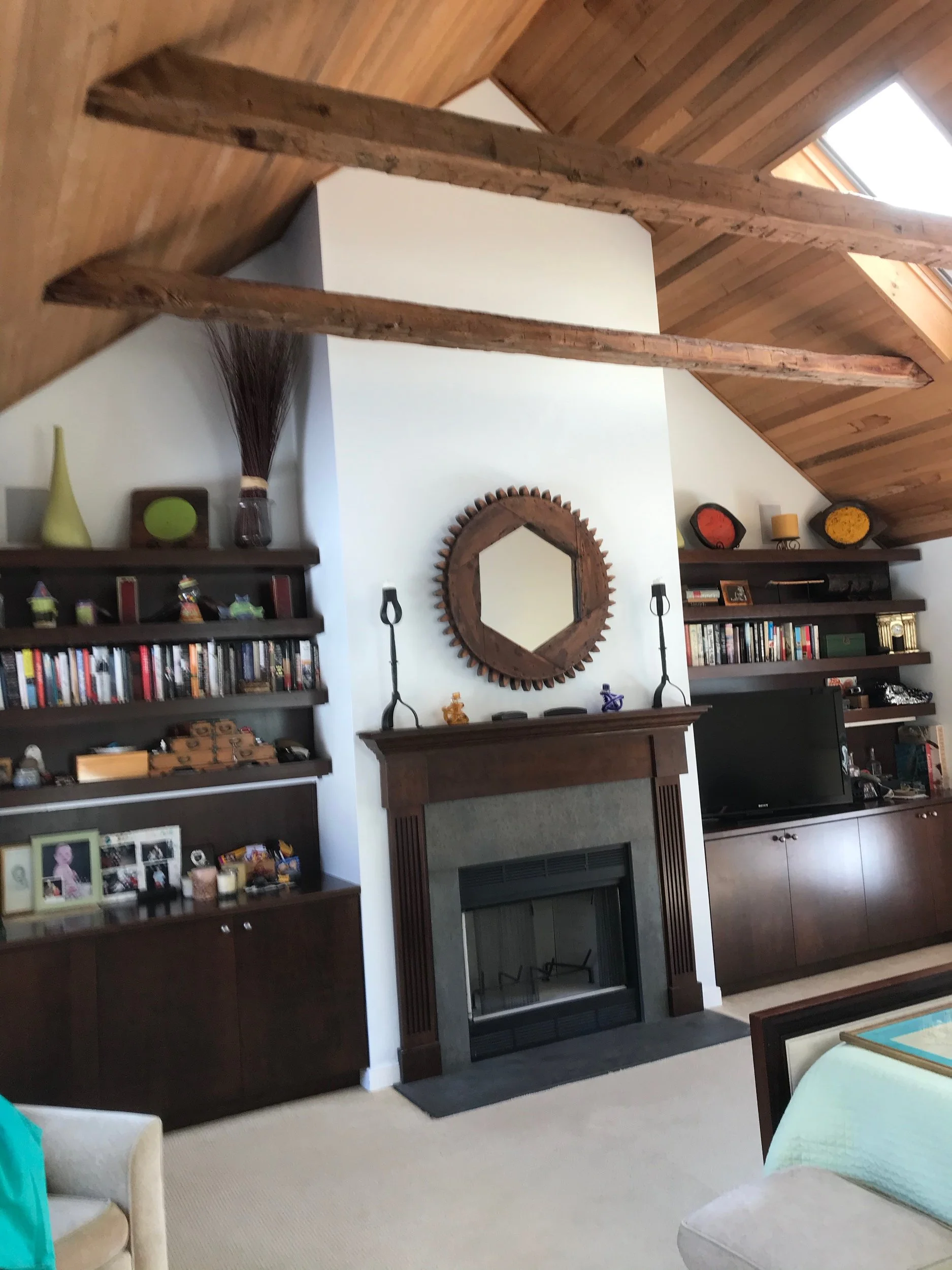 Living room with a fireplace, wooden beams on the ceiling, and shelves with books and decor items.