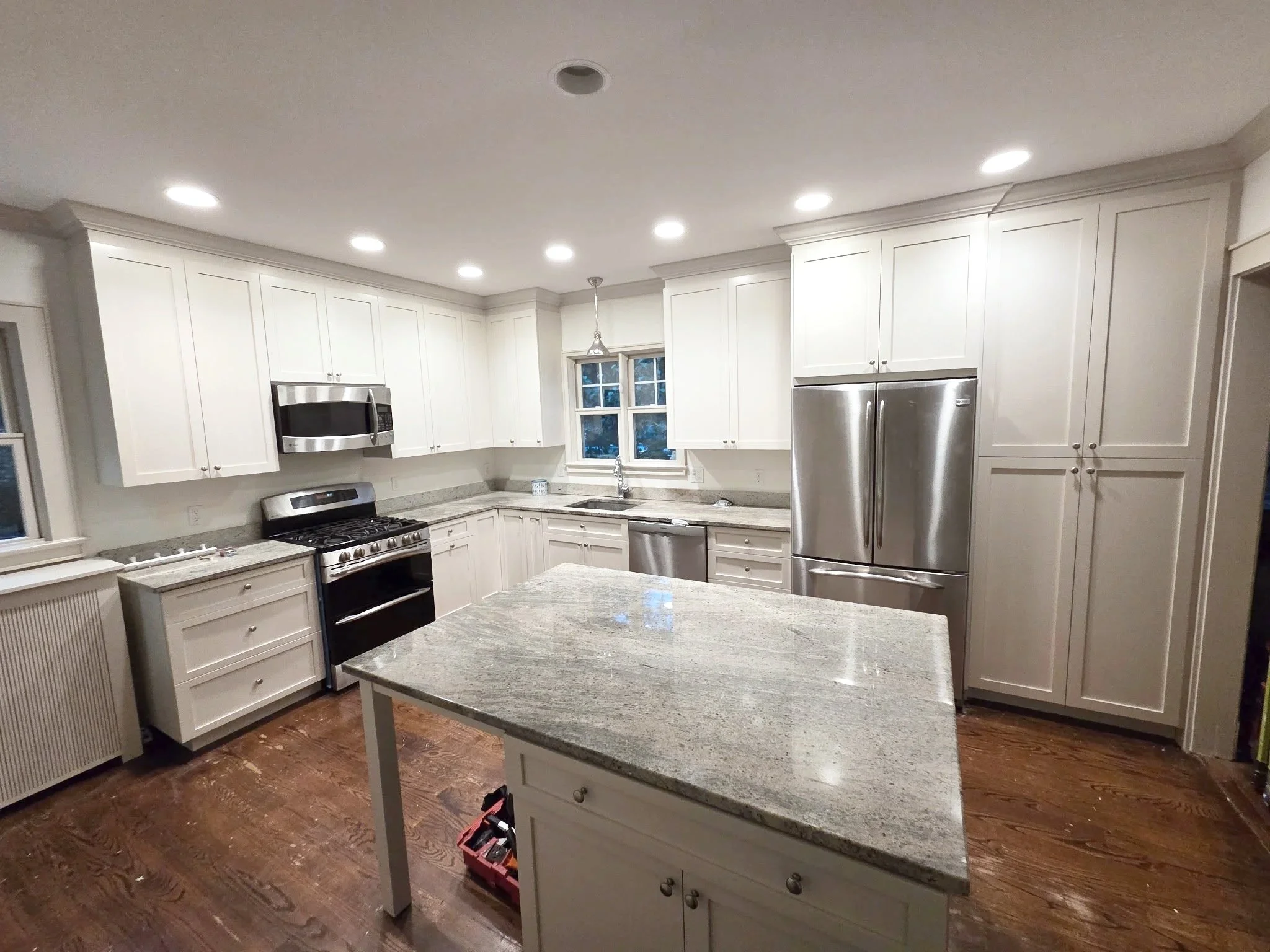 Modern kitchen with white cabinets, stainless steel appliances, granite countertops, a kitchen island, hardwood flooring, and recessed lighting.