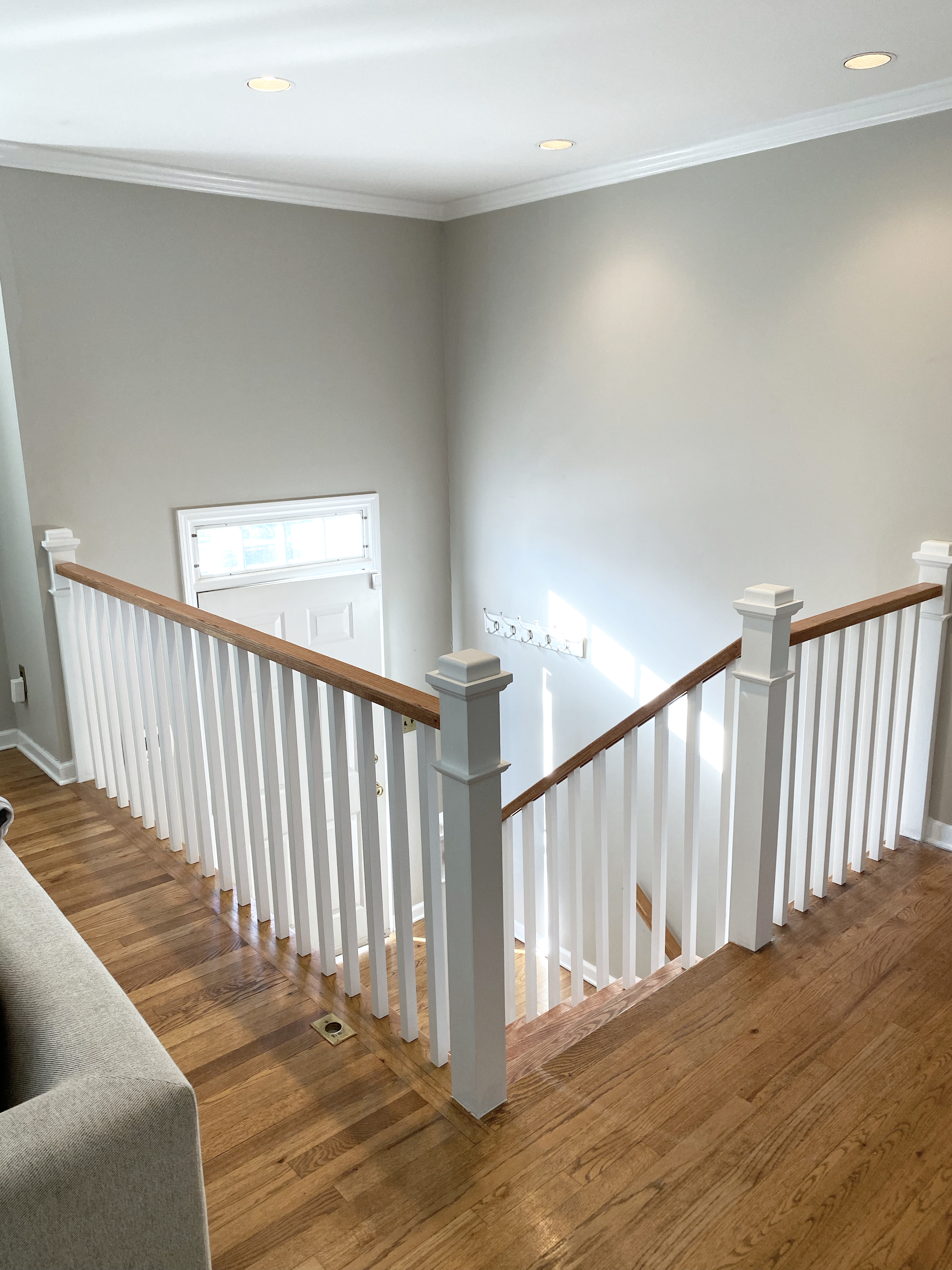 View of an indoor staircase with white railings and wooden handrail, overlooking a small foyer with a window and a coat rack on the wall.