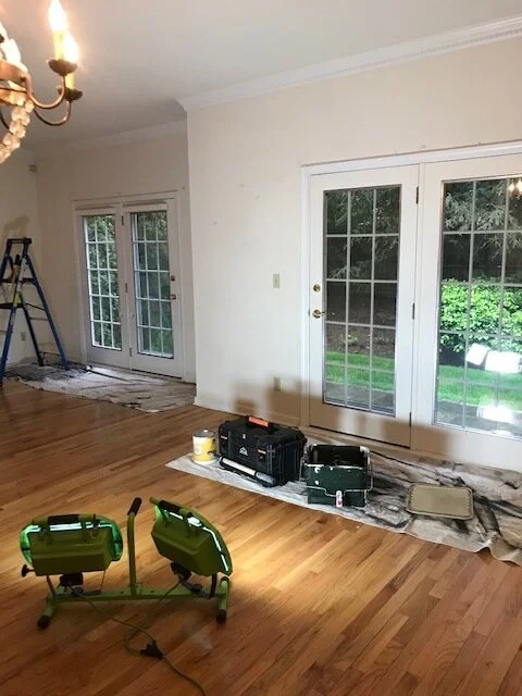 Living or dining room with sliding glass doors leading to a garden, some painting or renovation tools and equipment on the floor, and a ladder near the wall.