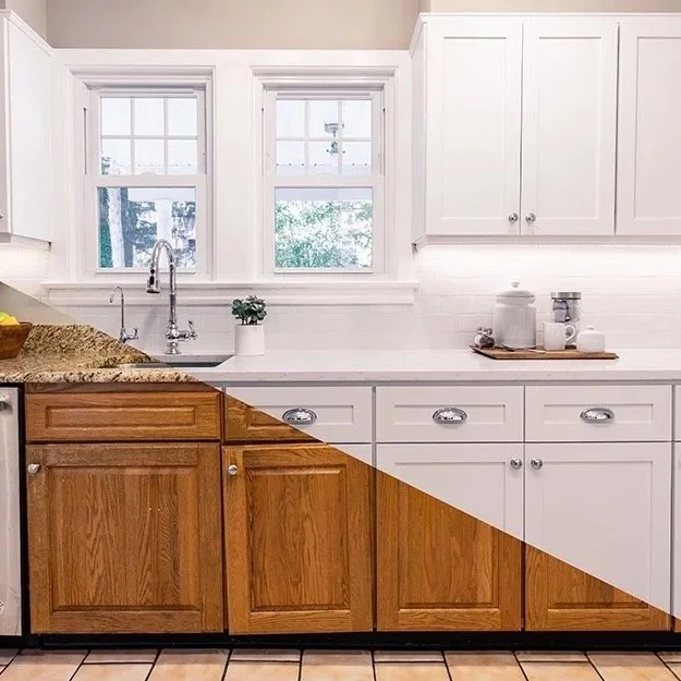 A kitchen with white upper and lower cabinets, a granite countertop, a stainless steel mini fridge, and a large window above the sink. The lower cabinets are partially painted white with some natural wood finish.
