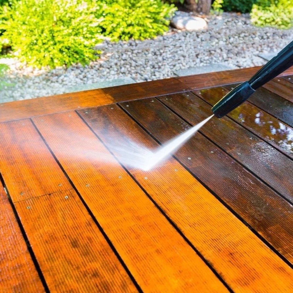 A pressure washer spray cleaning a wooden outdoor table, making the surface shiny and wet.