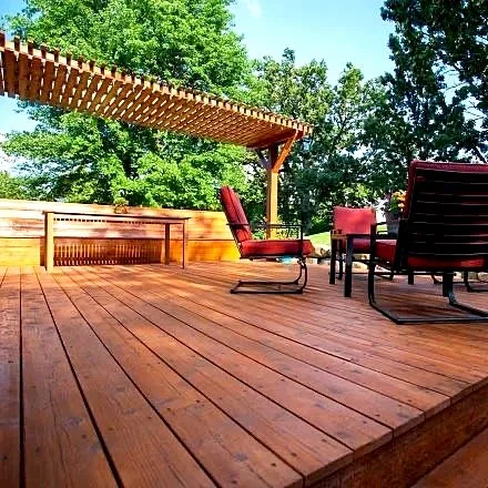 A wooden deck attached to a house with white railings and posts, surrounded by greenery and neighboring houses visible in the background.