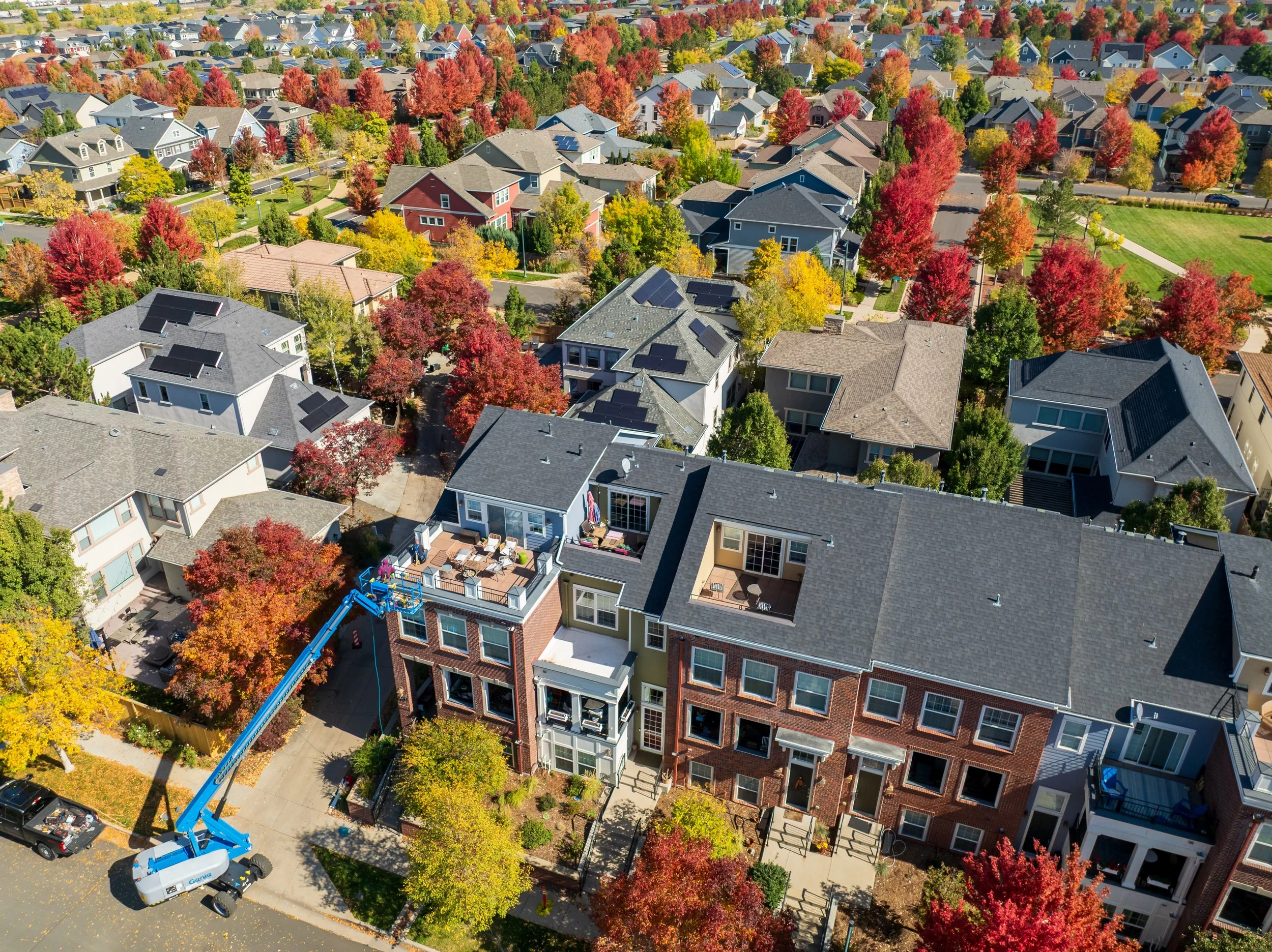 Aerial view of a neighborhood with colorful autumn trees, modern houses with solar panels, and a construction lift working on a building roof.