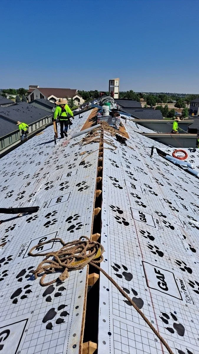 Roof workers installing underlayment on a roof on a sunny day.
