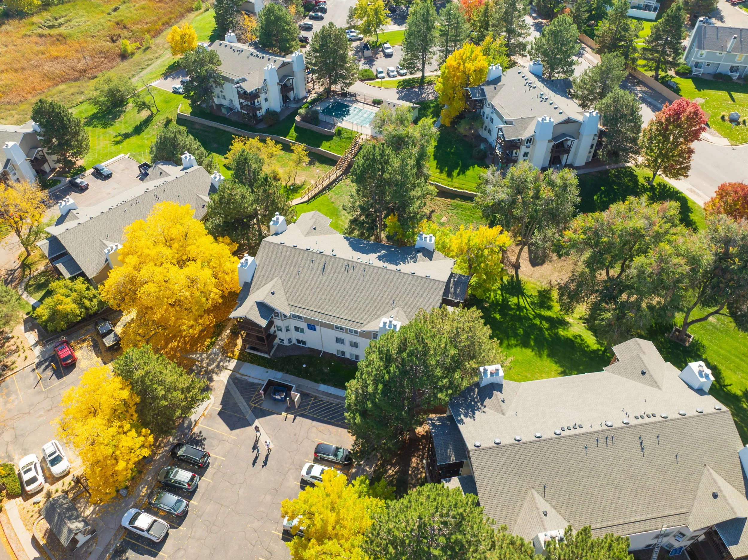 An aerial view of a residential apartment complex surrounded by trees with fall foliage, parking lots, and green lawns.