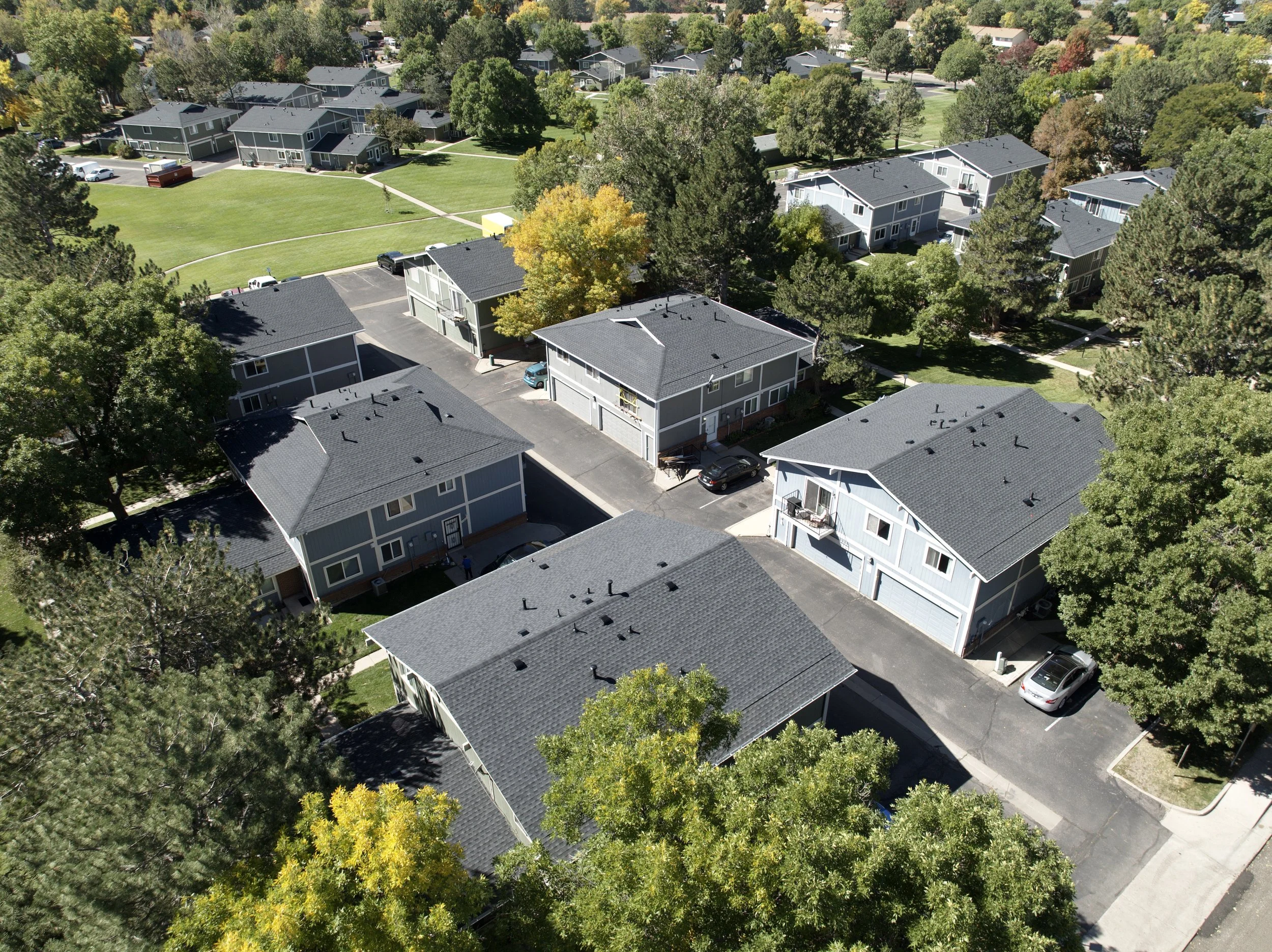 Aerial view of a residential neighborhood with multiple two-story houses, parking lots, and green trees scattered throughout.