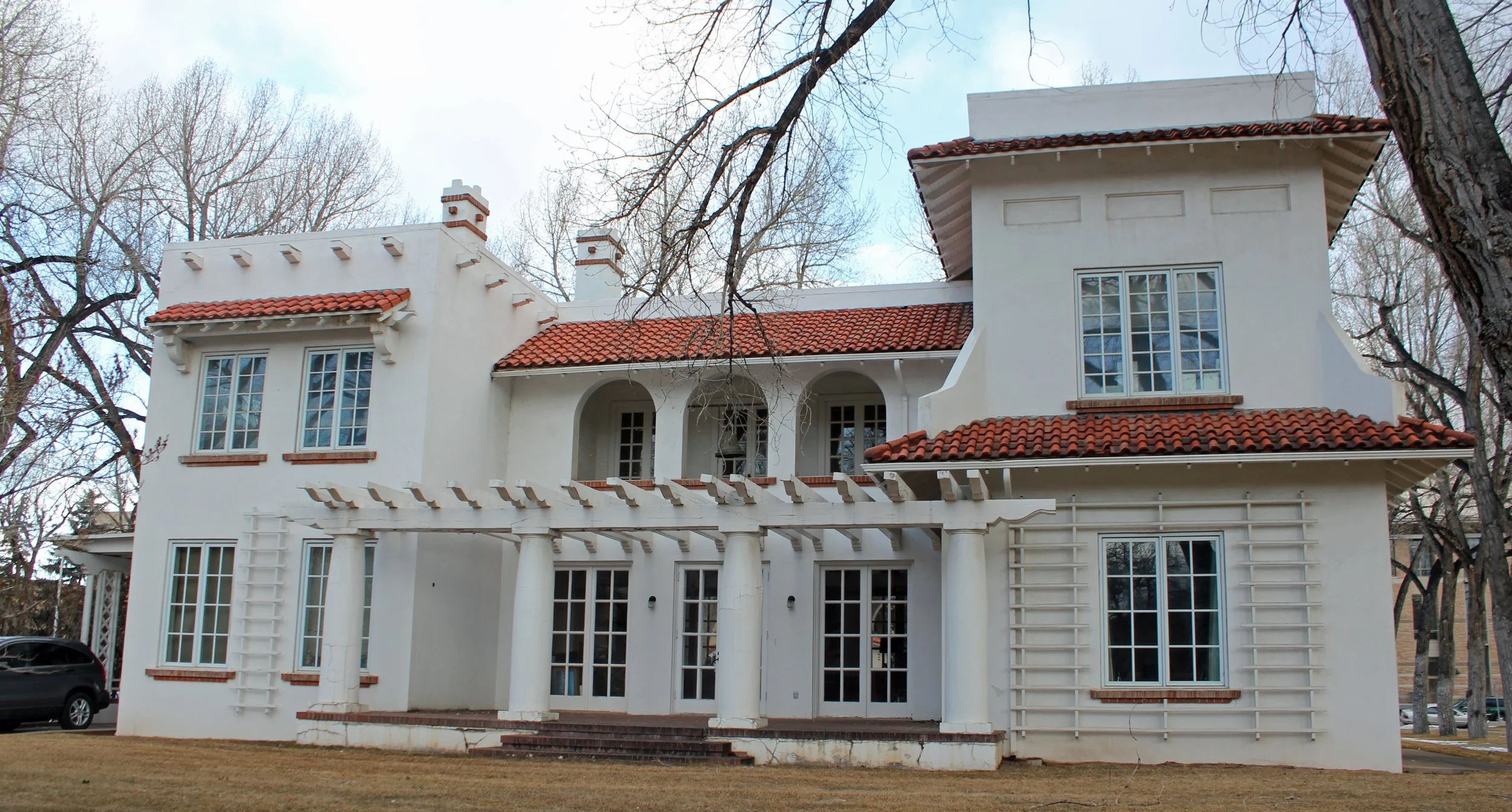 White house with red tile roof, multiple large windows, and arched entryway in a wooded area.