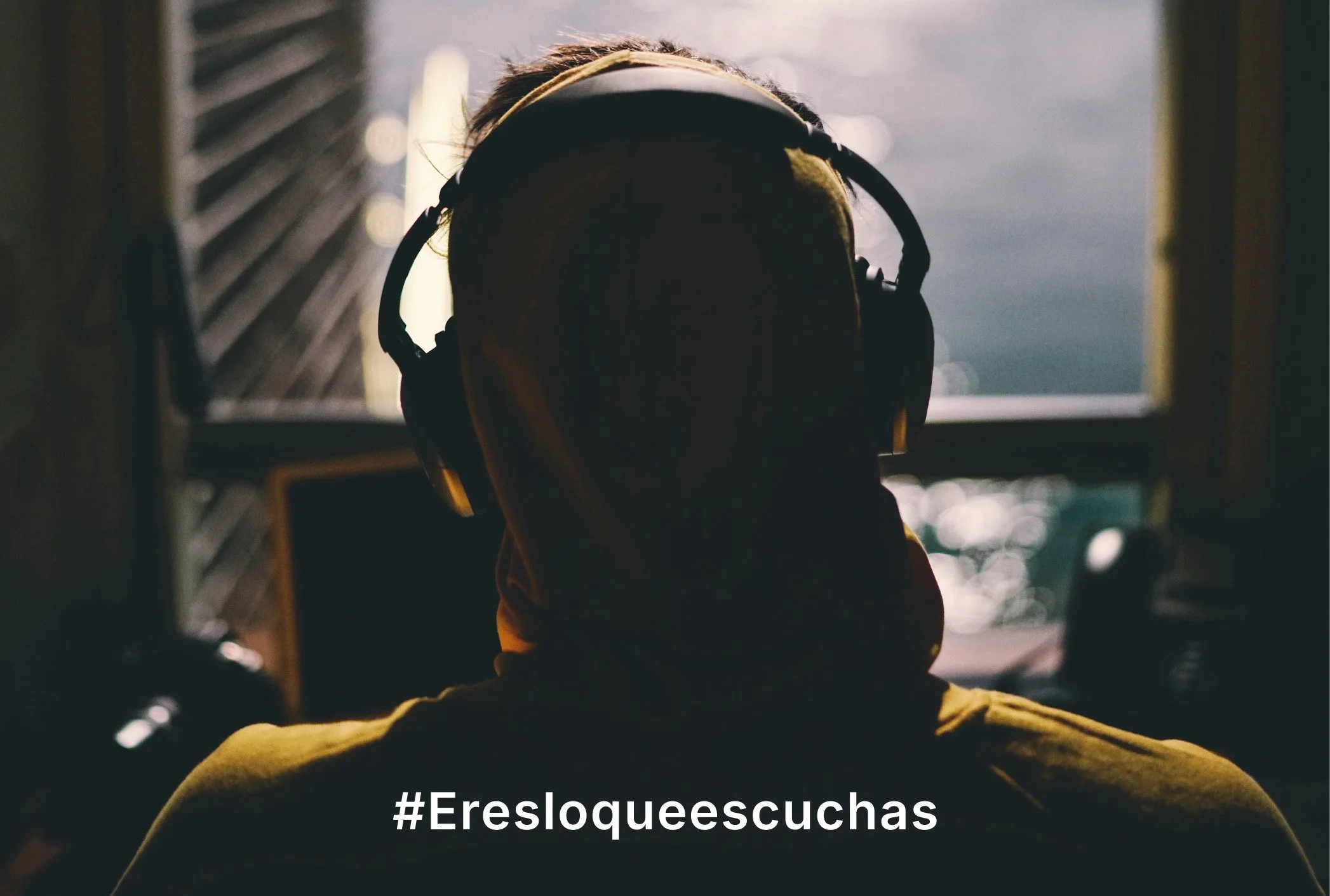 Persona con auriculares viendo una pantalla, en un espacio con luz tenue y fondo difuso. Incluye la leyenda '#Eresloqueescuchas'_ONE BEAT PROJECT_campaña identidad grafica de estudio berlin