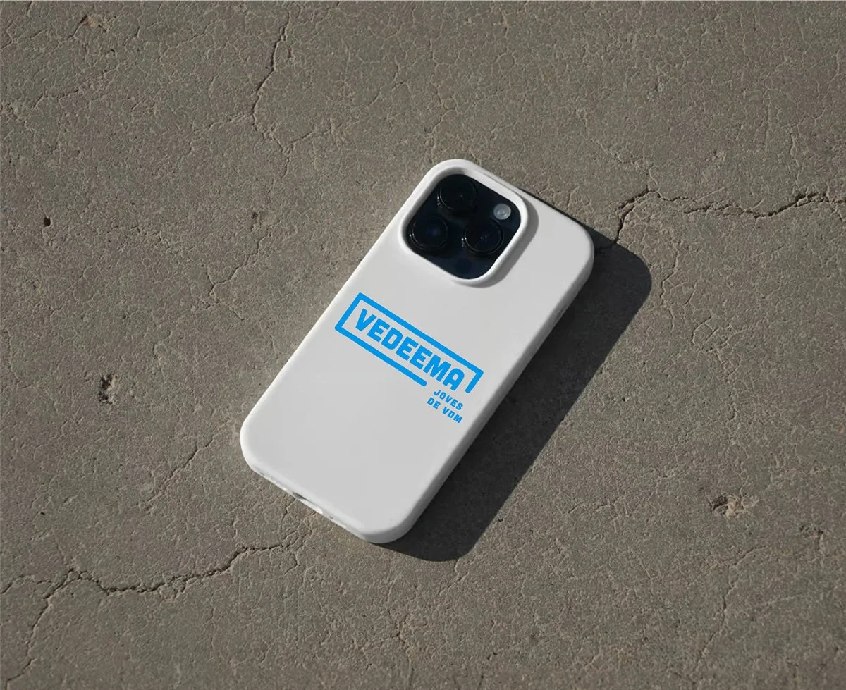 Teléfono inteligente en una superficie de concreto con un sticker azul que dice 'VEDEEMA JOVES DE VDM'_campaña identidad grafica de estudio berlin