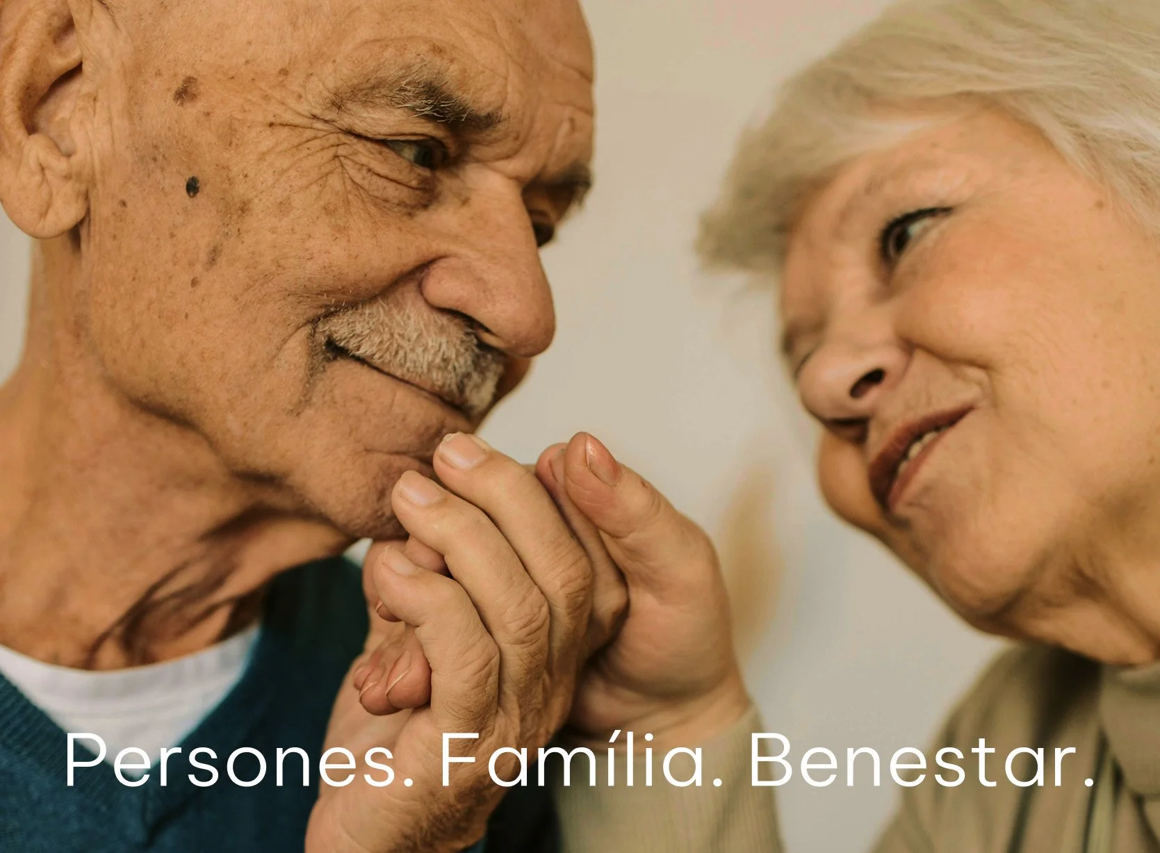 Una pareja de adultos mayores comparte un momento afectuoso, sosteniéndose de las manos y mirando con cariño, en un ambiente cálido_Llar carme_premia de mar_diseño identidad de estudio berlin