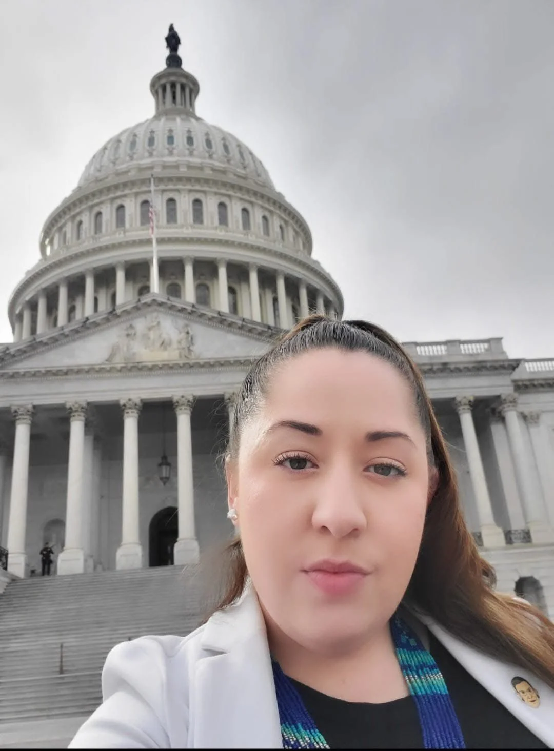 Justine Sandova taking a selfie in front of the United States Capitol building on a cloudy day.