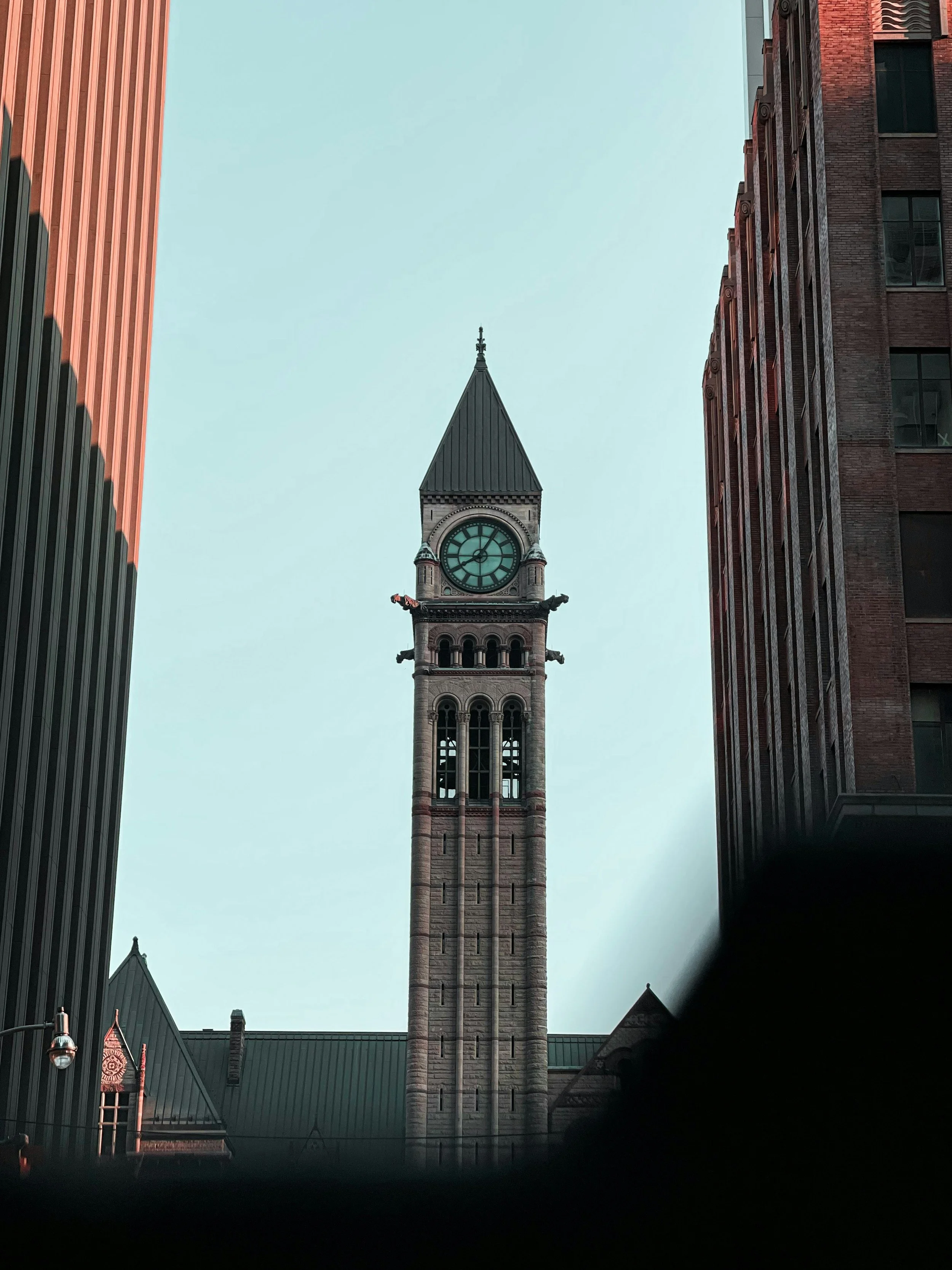 A historic clock tower in an urban setting, surrounded by modern high-rise buildings, with a clear sky in the background.
