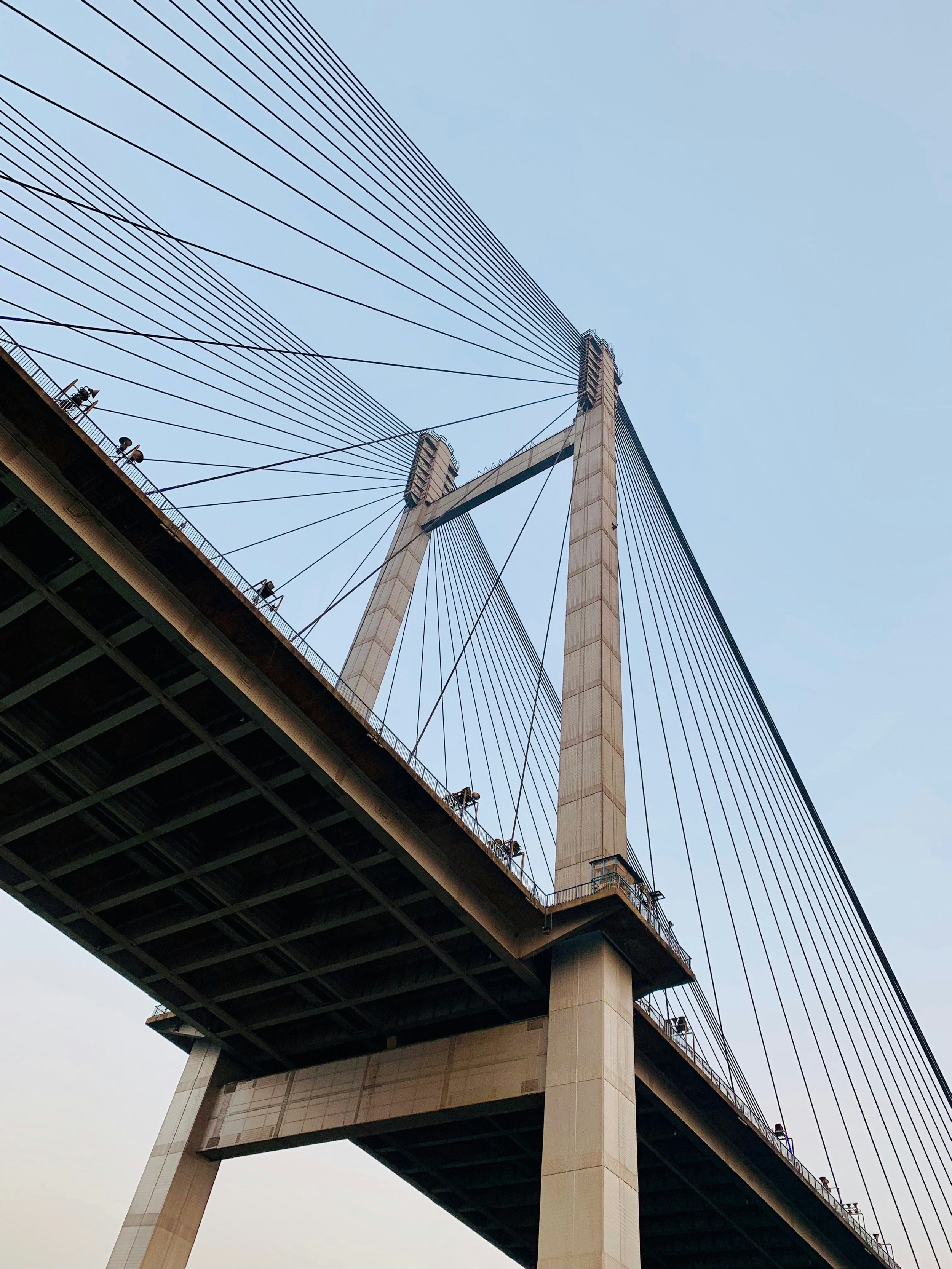 Looking up at the Brooklyn Bridge in New York City from below, showing the suspension cables and stone towers against a clear blue sky.