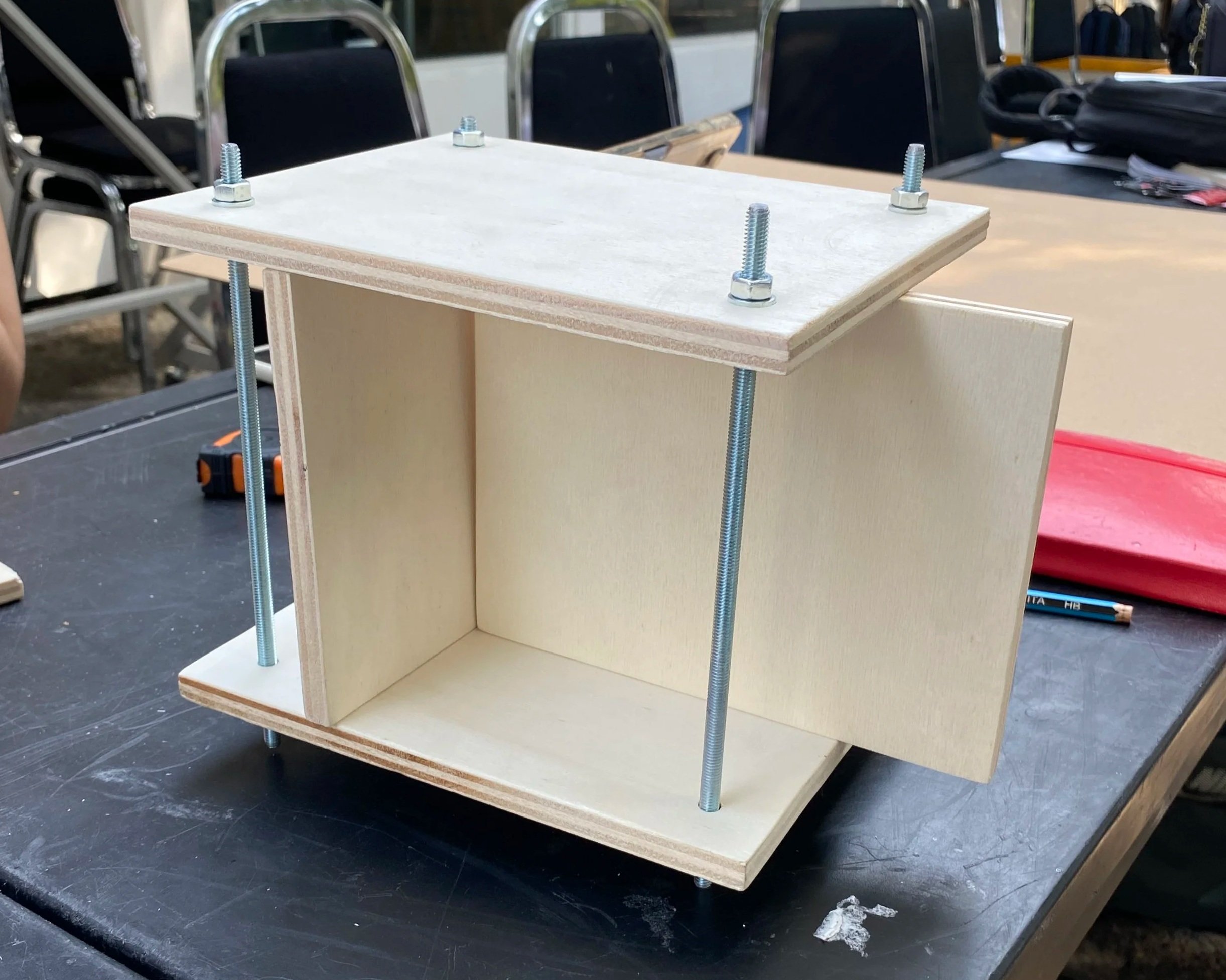 Modello in legno di una struttura a forma di scatola con pannelli e viti metallici.