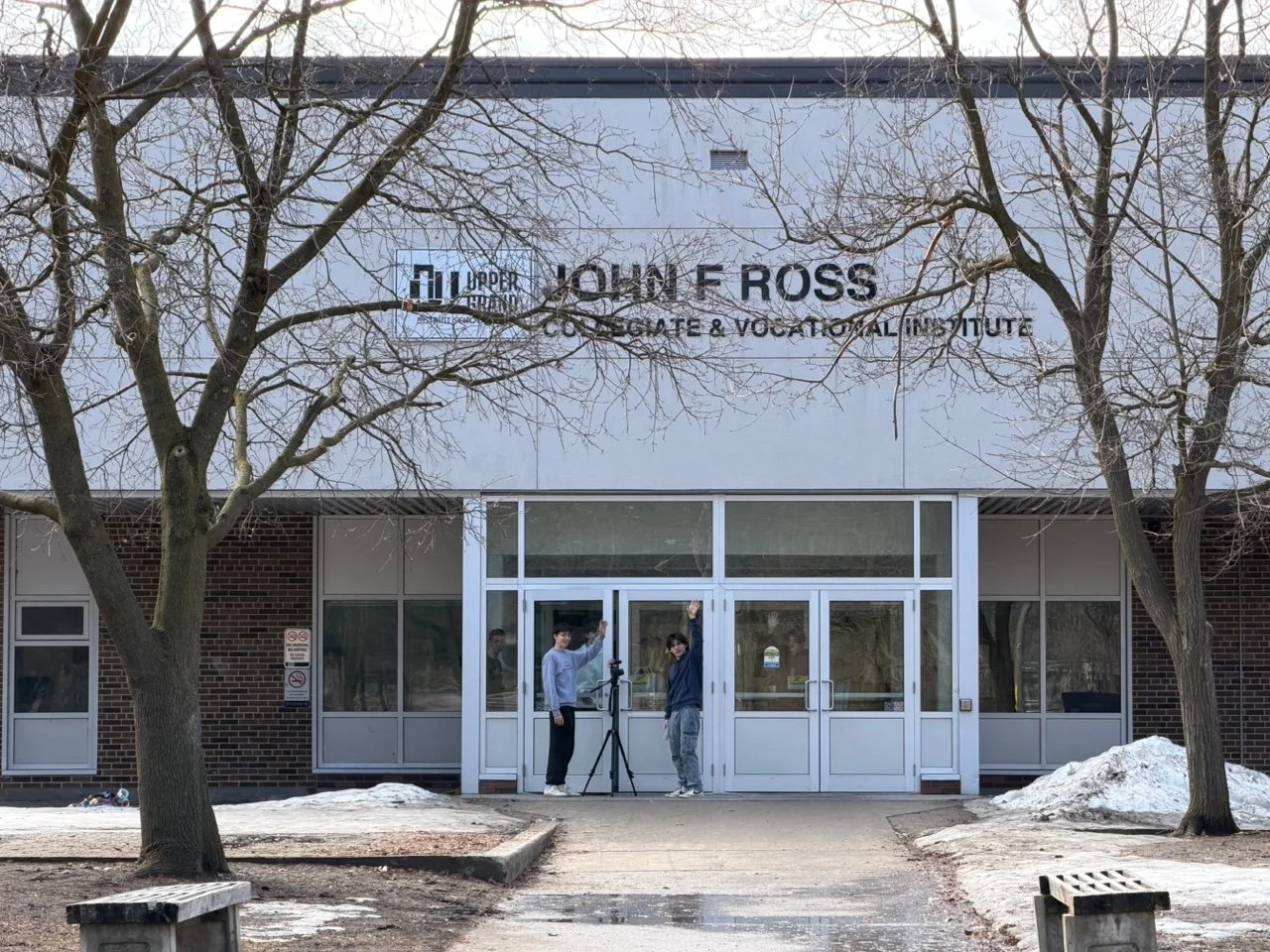 Exterior of the Upper Iowa Youth F. Ross building with two students standing in front, one waving. There are leafless trees and patches of snow on the ground.