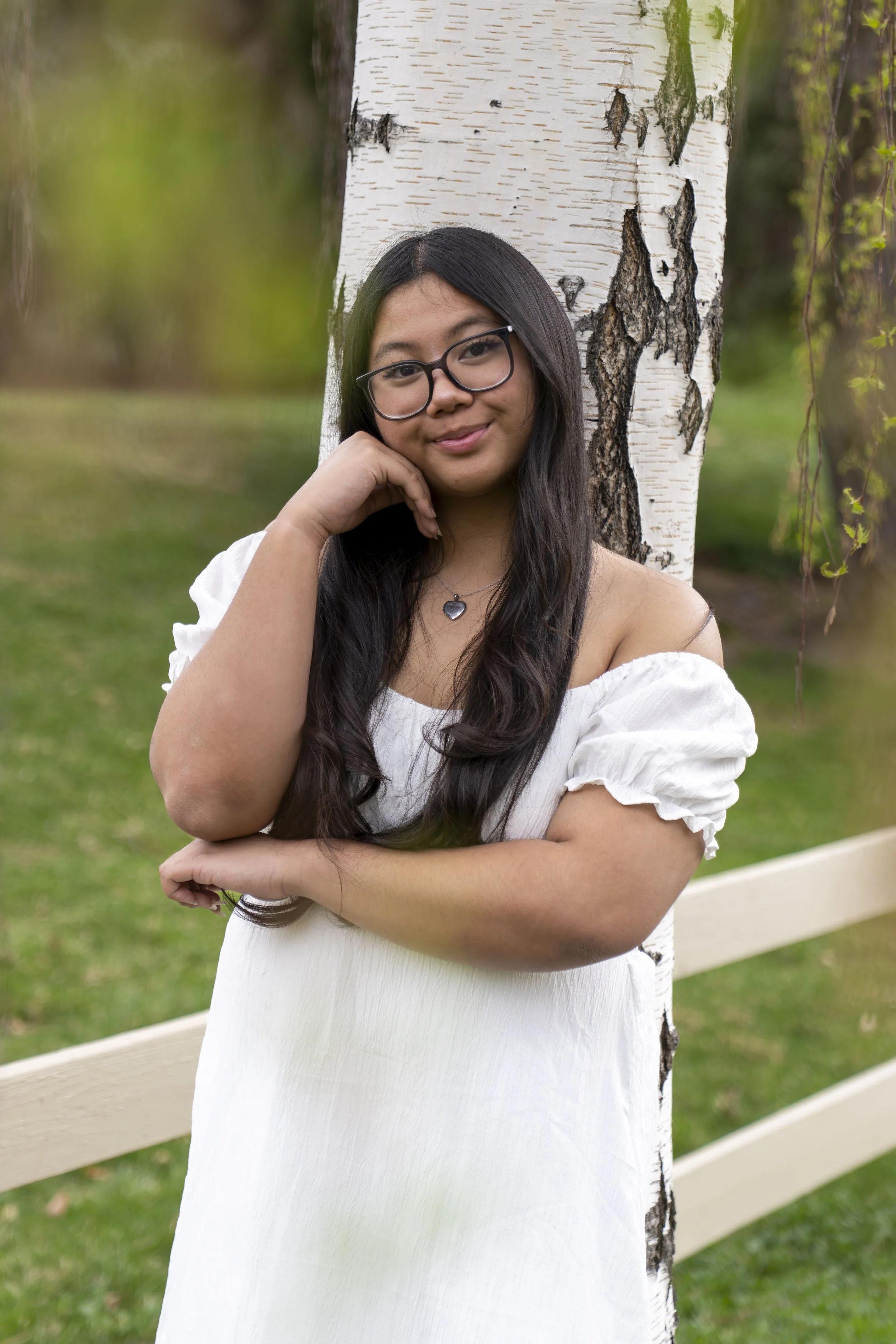 A young lady poses against a birch tree.