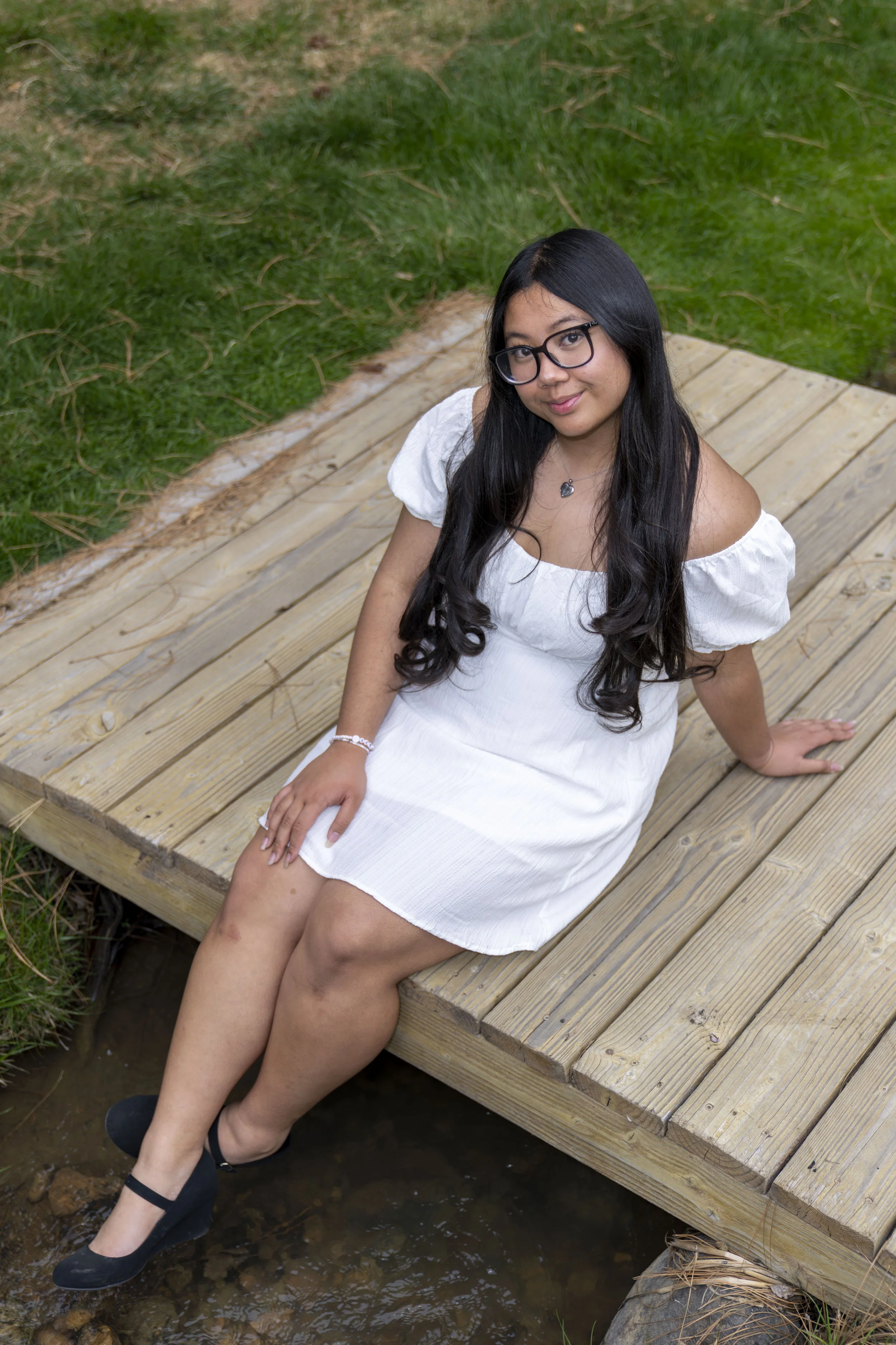 A young lady poses on a wooden bridge.