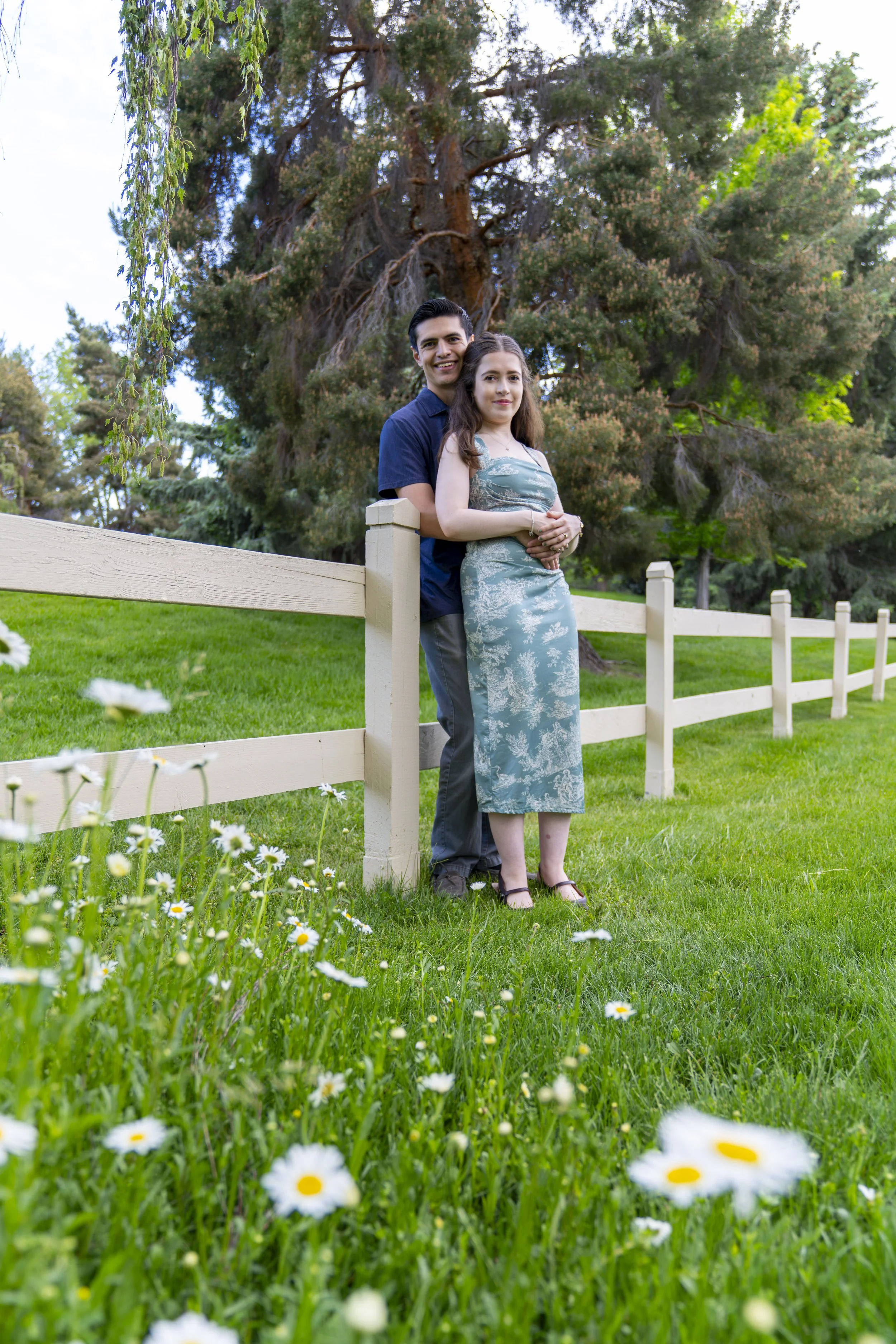 A young couple embraces each other for an engagement photoshoot in a field of white flowers.