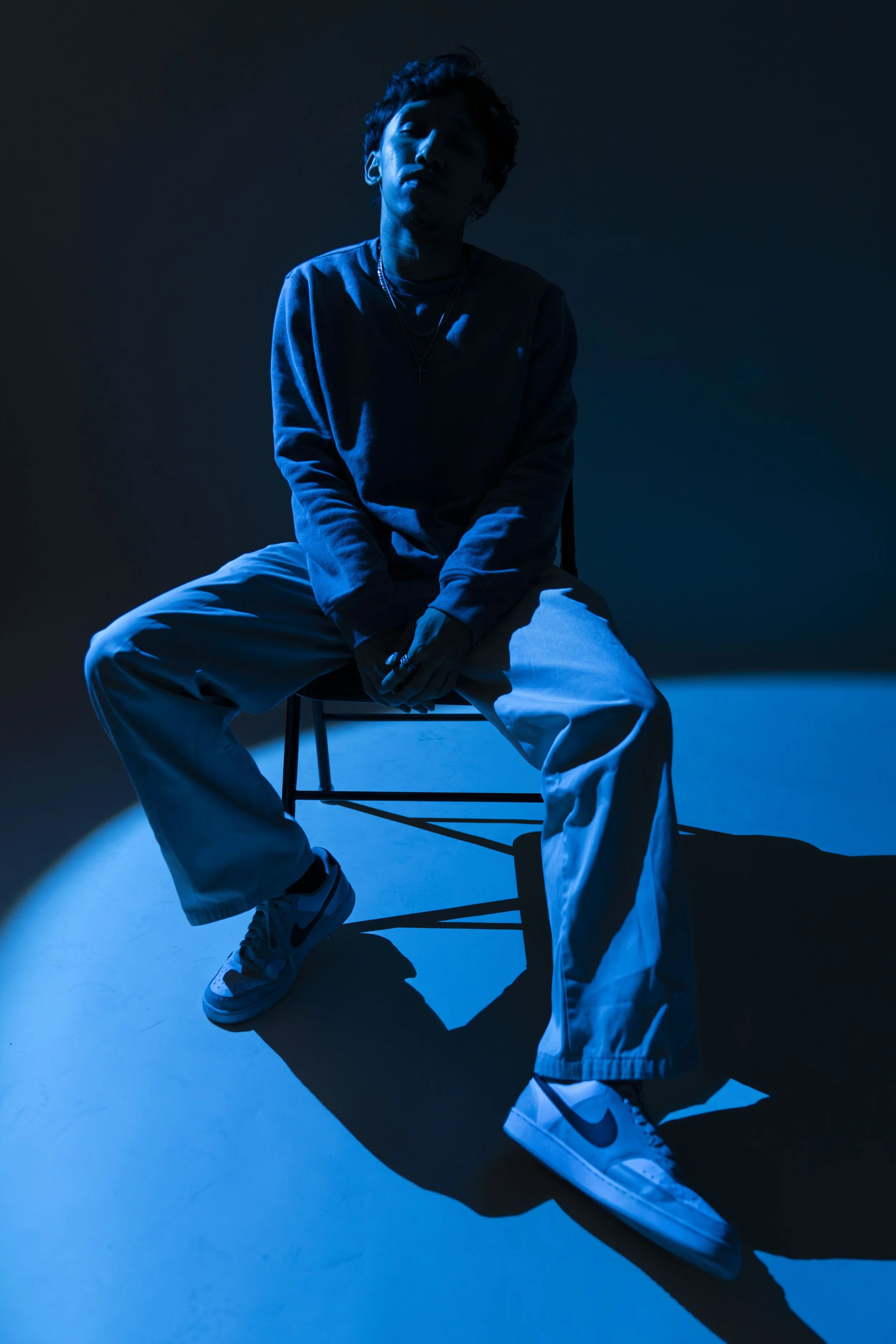A lyricist poses in a chair brightened by a blue light.