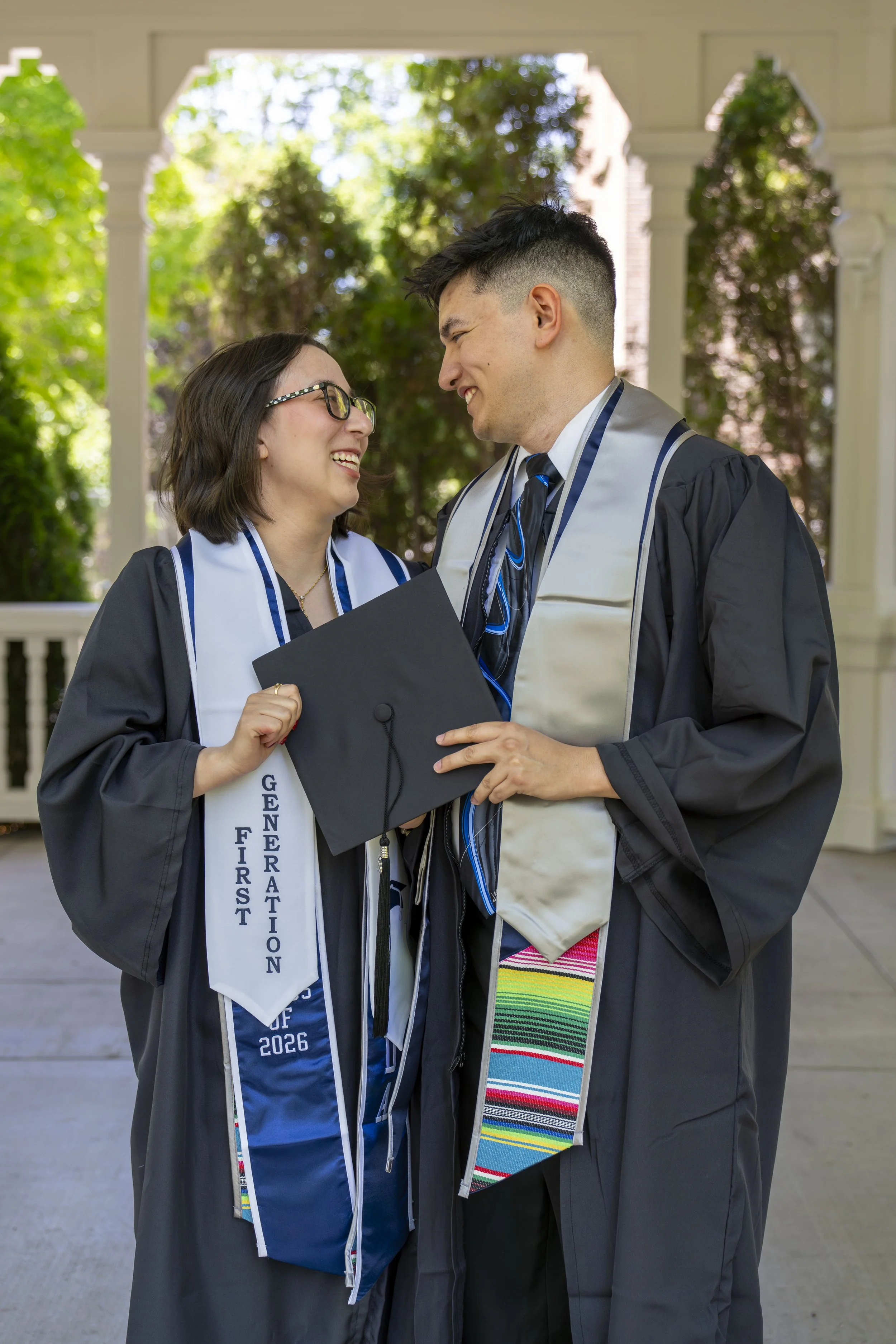A couple shares a smile as they pose in their graduation attire.