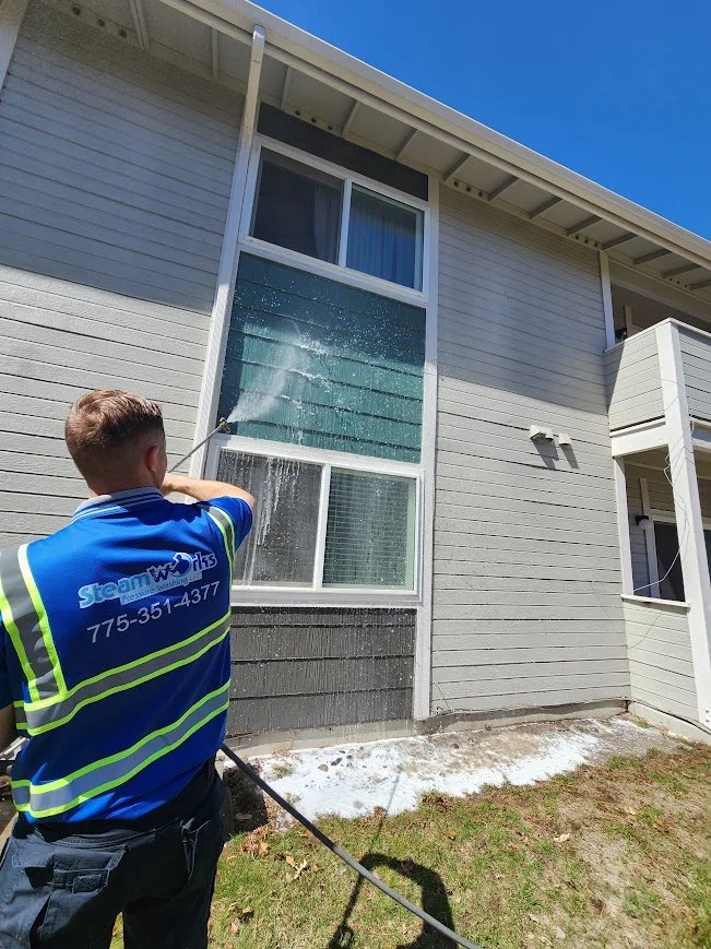 Man pressure washing the exterior of a light gray multi-story house.