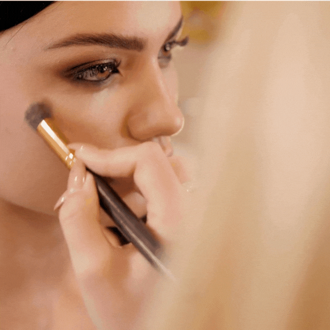 Close-up of a woman applying makeup with a brush on her cheek