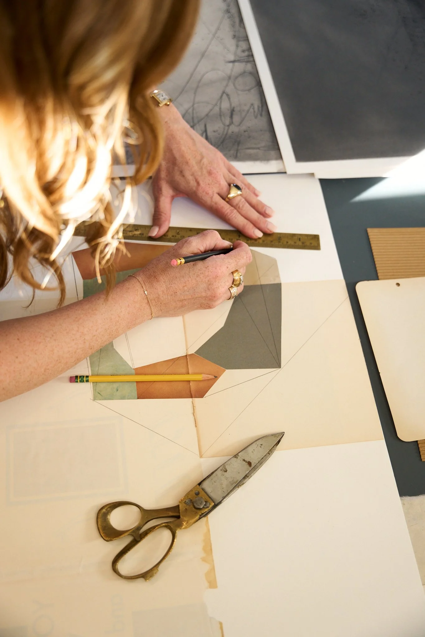 A person measuring and marking a geometric drawing on paper with a ruler, using a pencil, with scissors nearby, on a table.