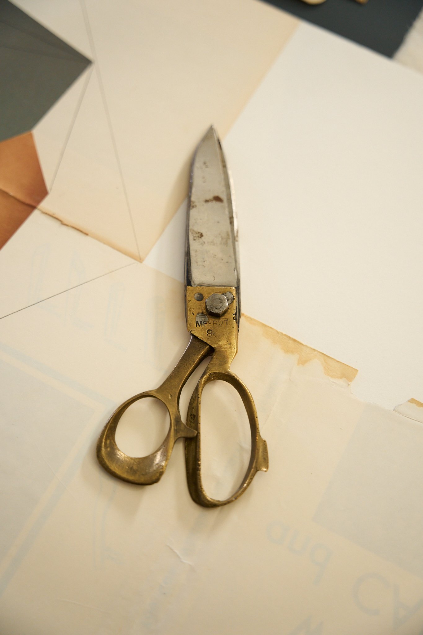 A pair of old, tarnished scissors with a gold handle lies on a white surface, with some fabric pieces surrounding it.