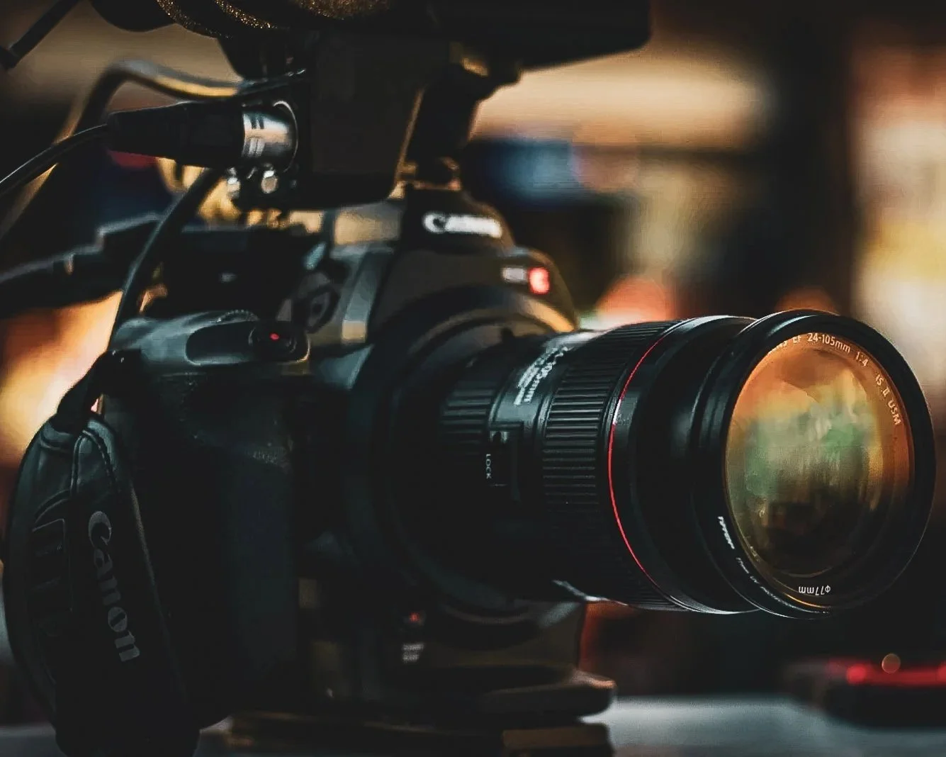 A professional Canon camera with a zoom lens mounted on a tripod, in a dimly lit environment.