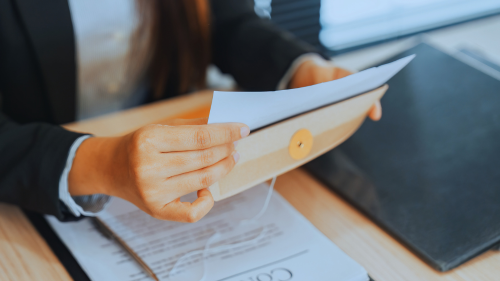 Person holding papers over a desk with documents and a laptop.