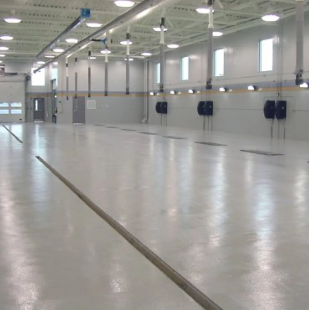 Empty industrial or warehouse space with smooth floors, high ceilings, windows, and industrial lighting.