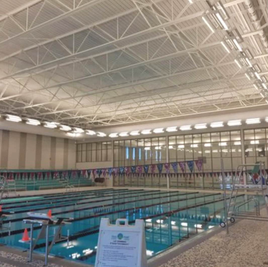 Indoor swimming pool with lane markers, colorful flags, and a lifeguard stand at the edge.