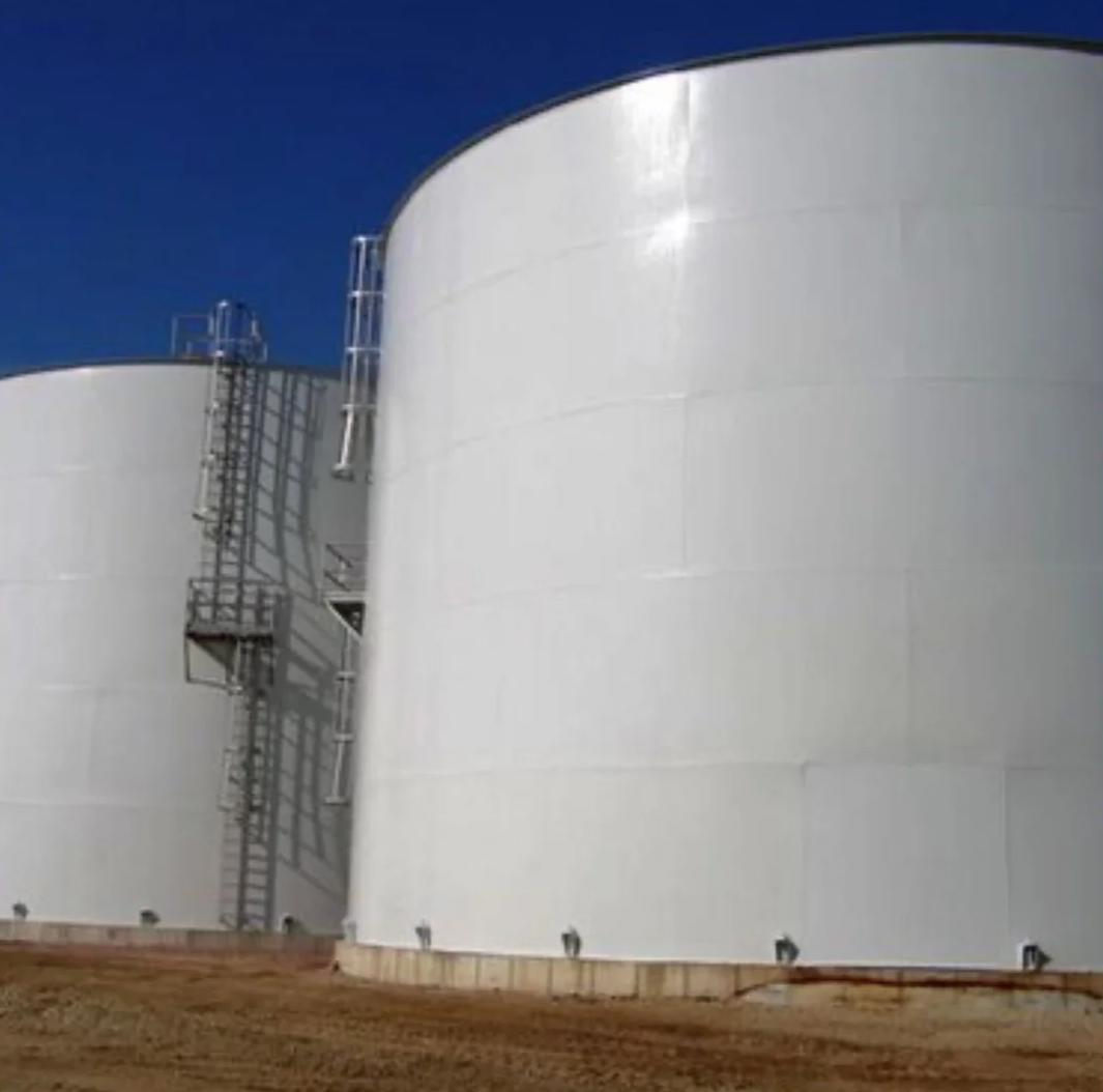 Large white industrial storage tanks with metal stairs and ladders against a clear blue sky.