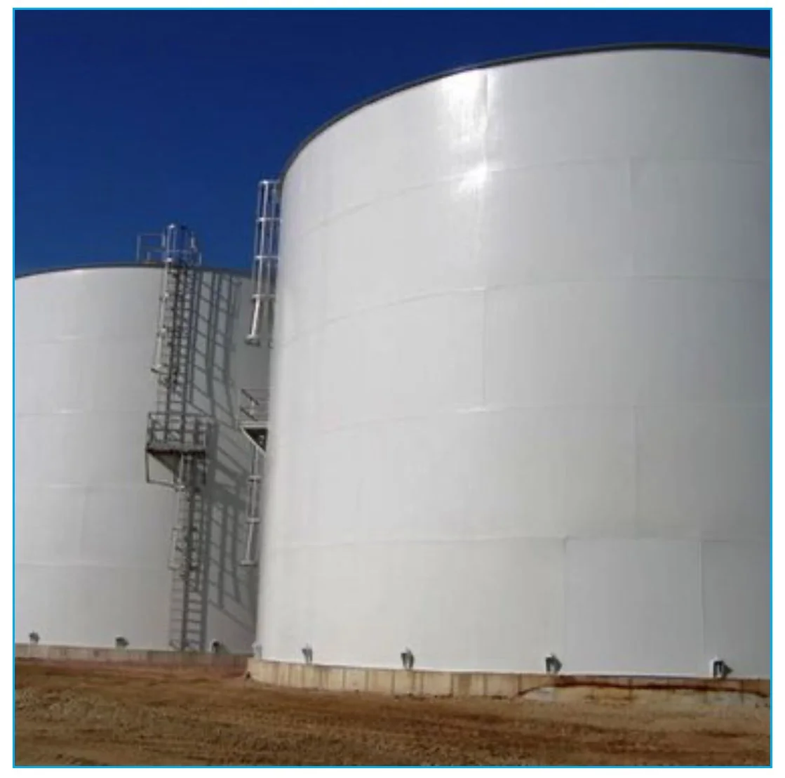 Large white industrial storage tanks with metal stairs and ladders against a clear blue sky.