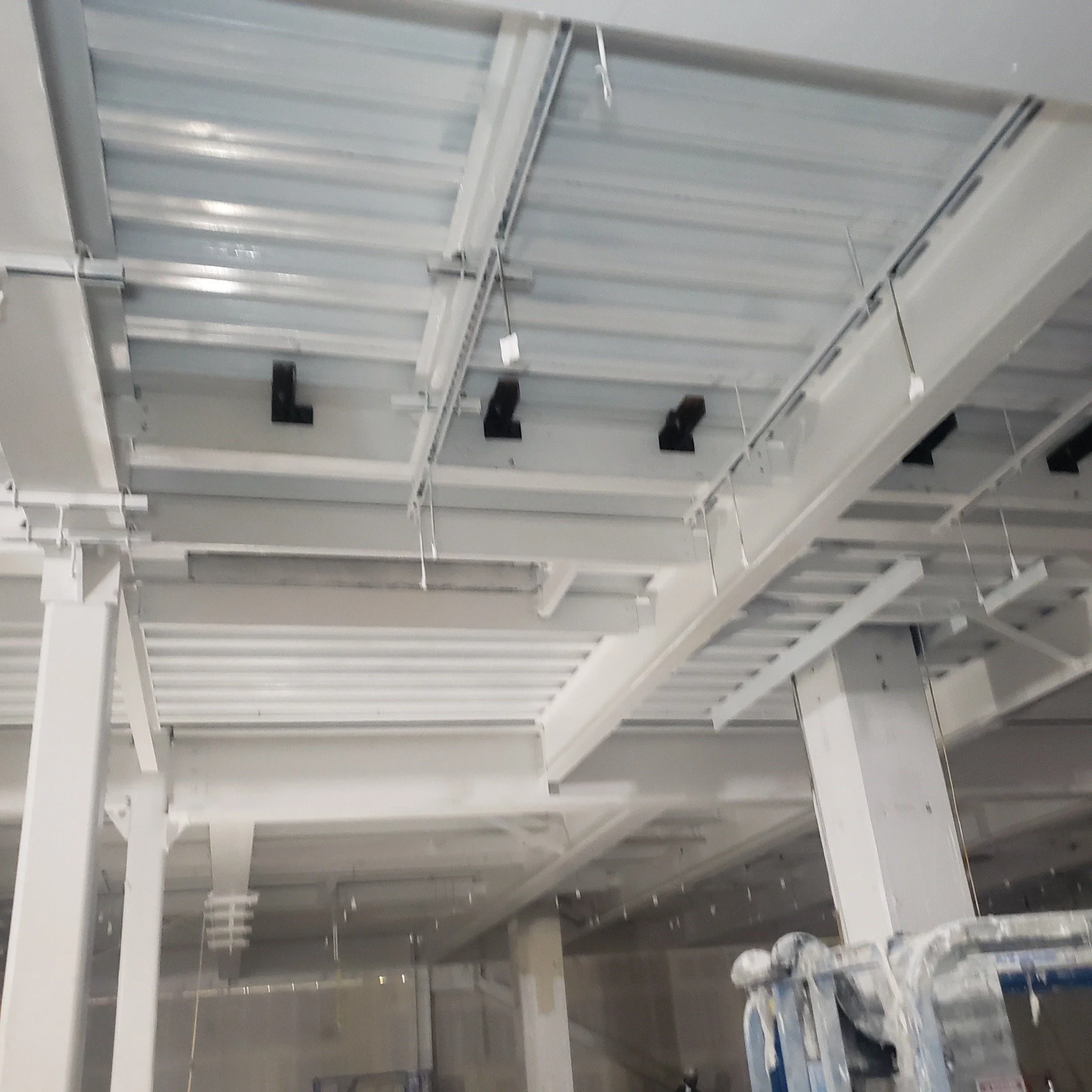 Construction site ceiling with metal framework, beams, and black spotlights.
